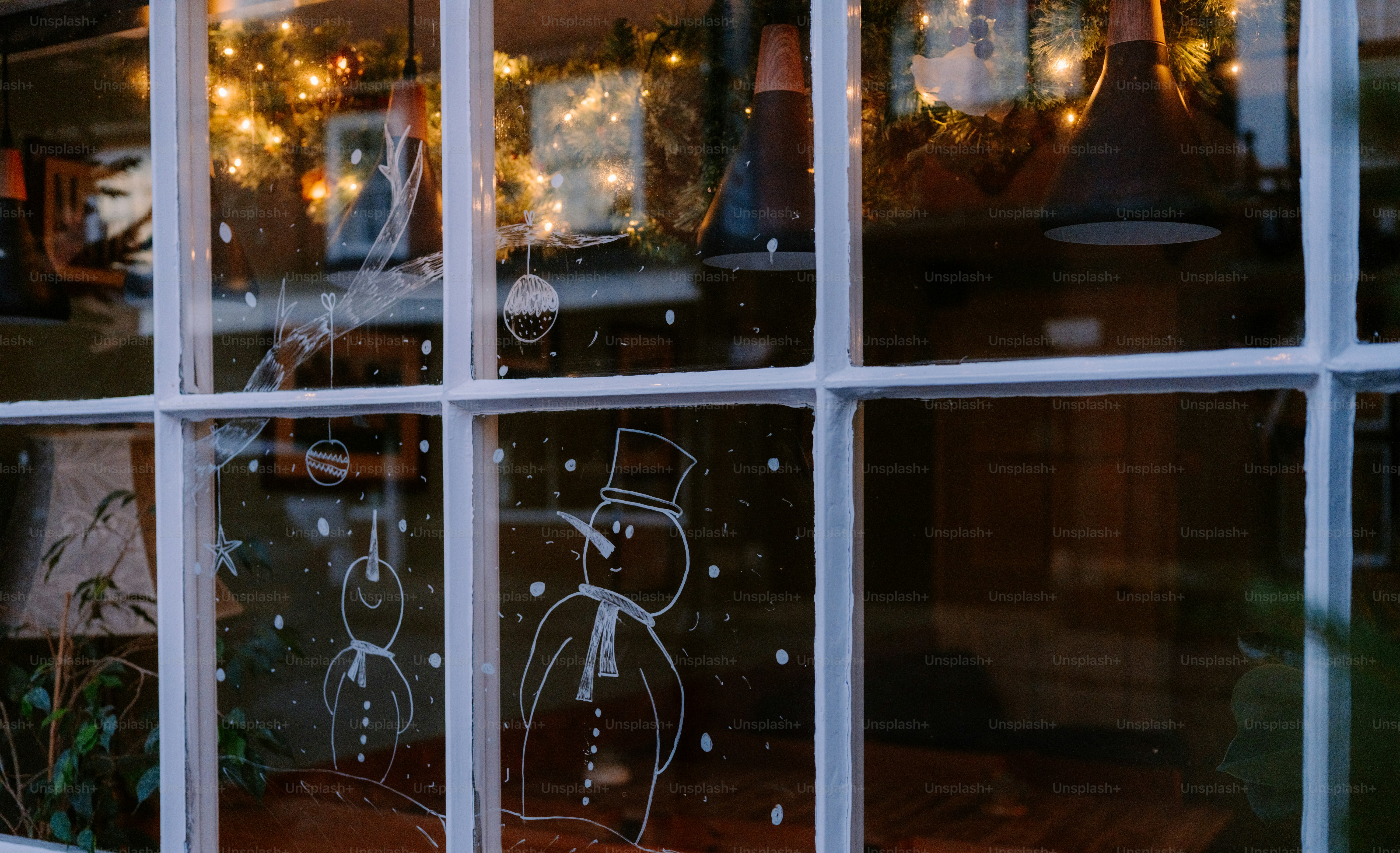 Schneemann-Zeichnungen an einem Fenster mit Weihnachtslichtern