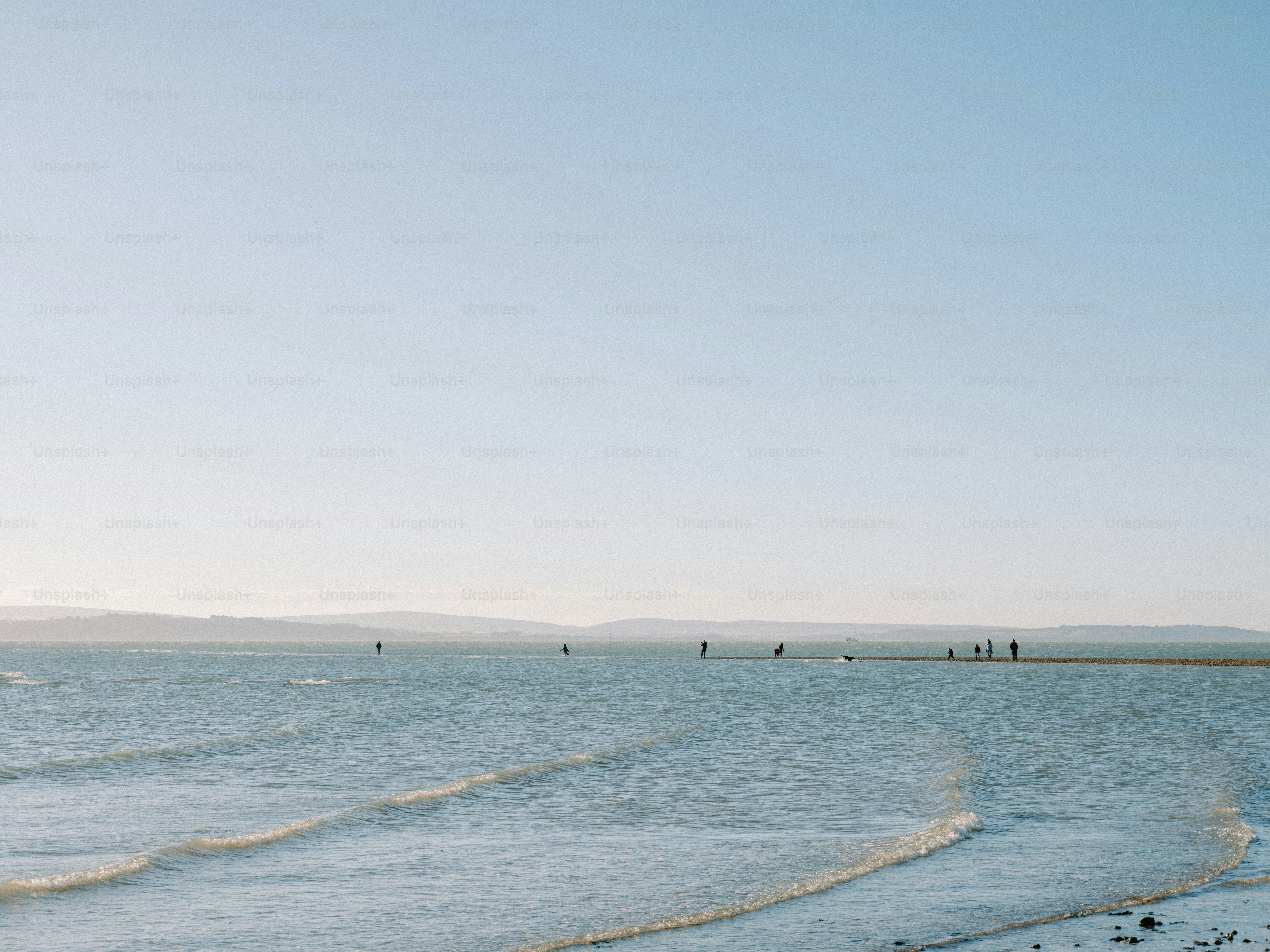 People walking on a sandbar in calm ocean water