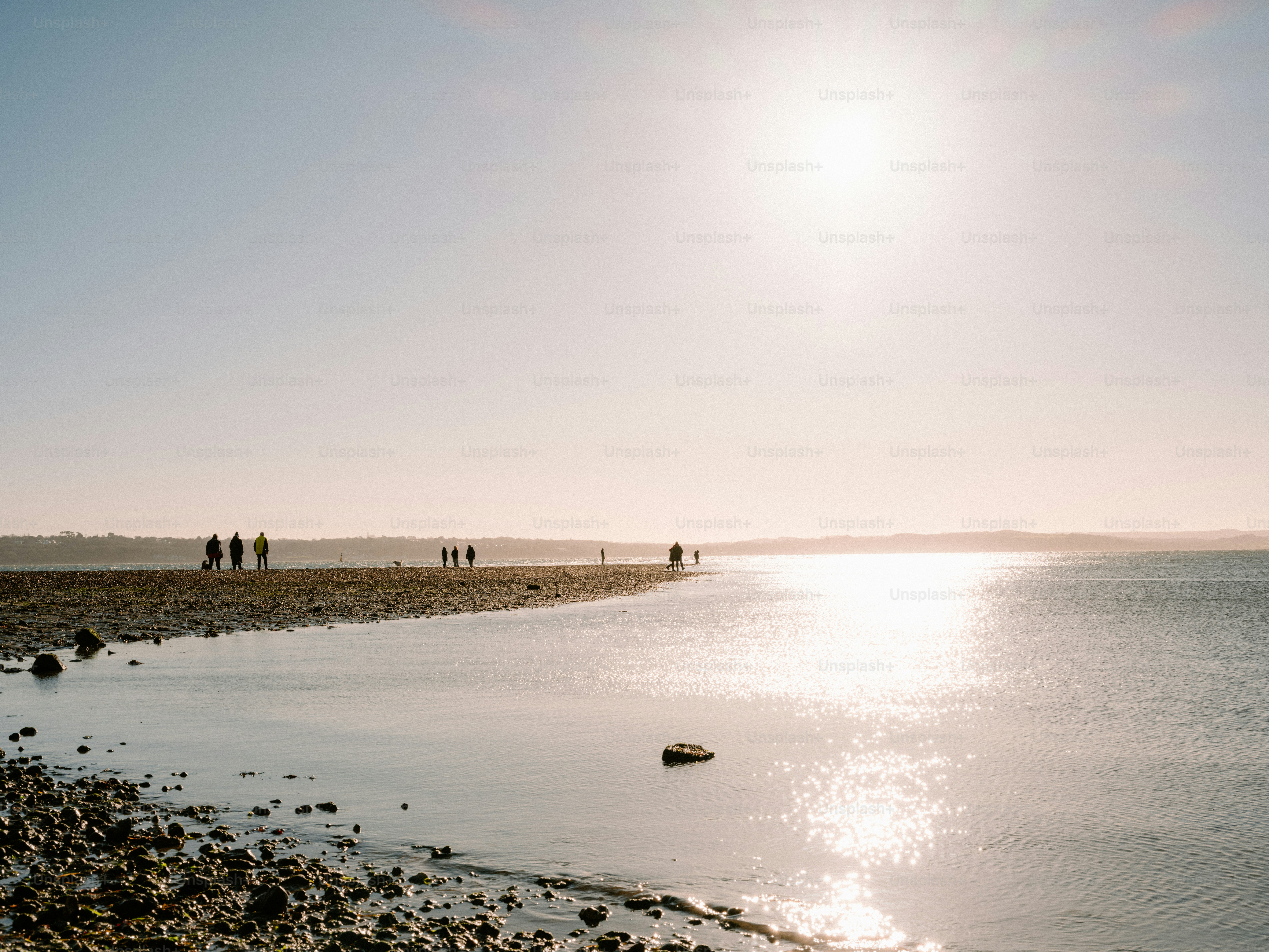 People walk along a sunny beach with calm water.