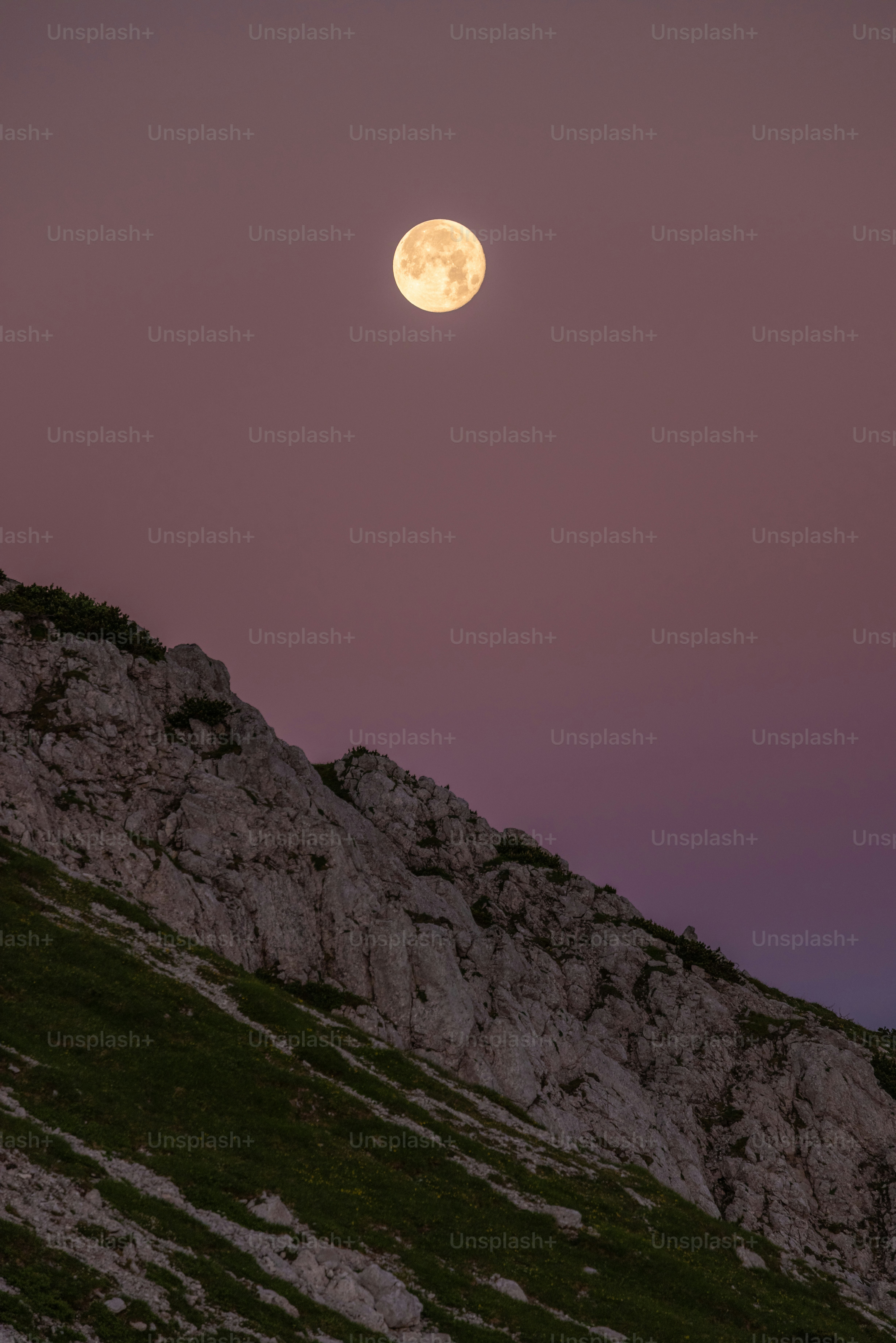 Full moon rises over a rocky mountain slope.