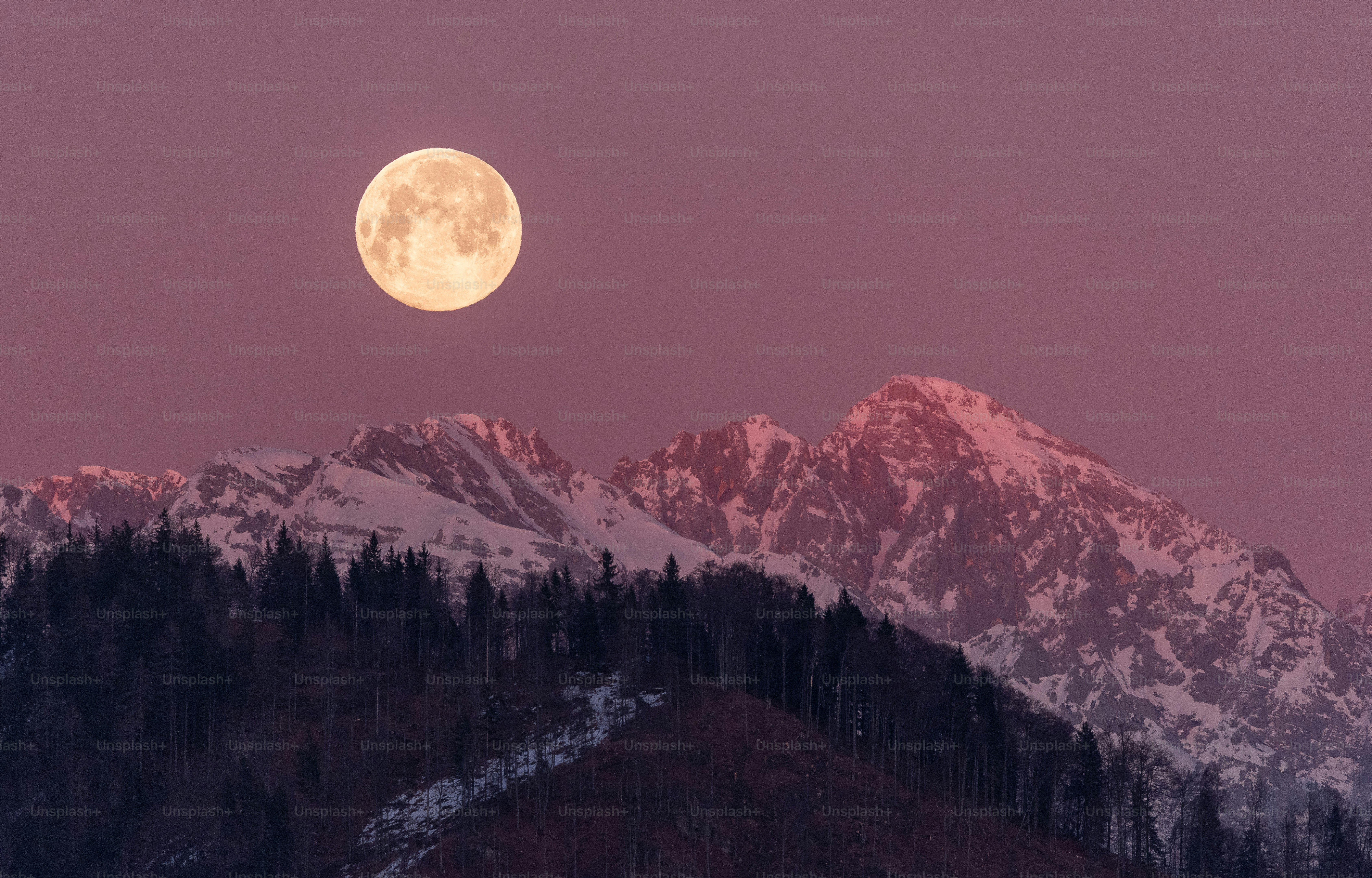 Full moon over snow-capped mountains at dusk