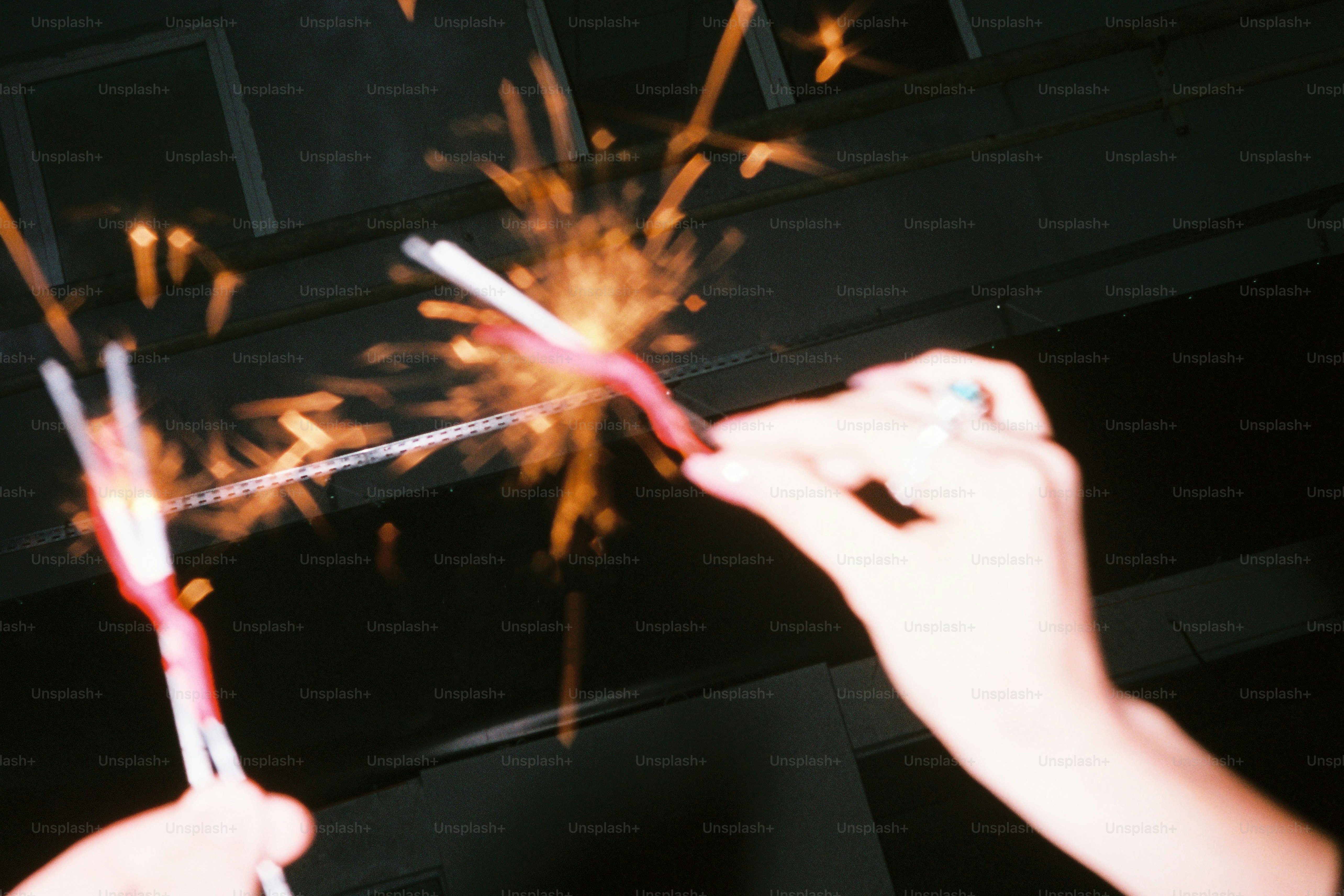 Hands holding lit sparklers with sparks flying sparks.