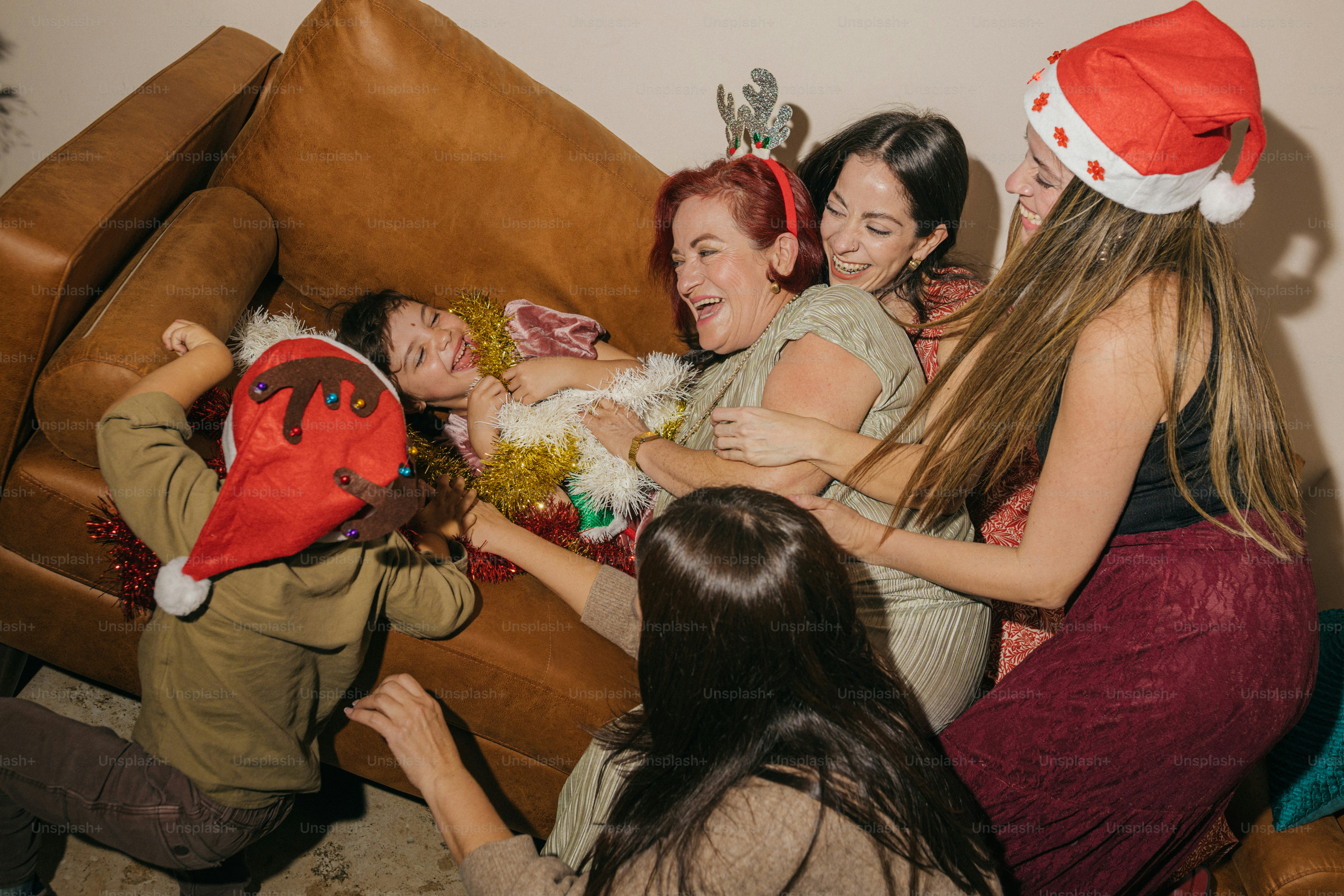Familie lacht und spielt auf der Couch mit Weihnachtsmützen.