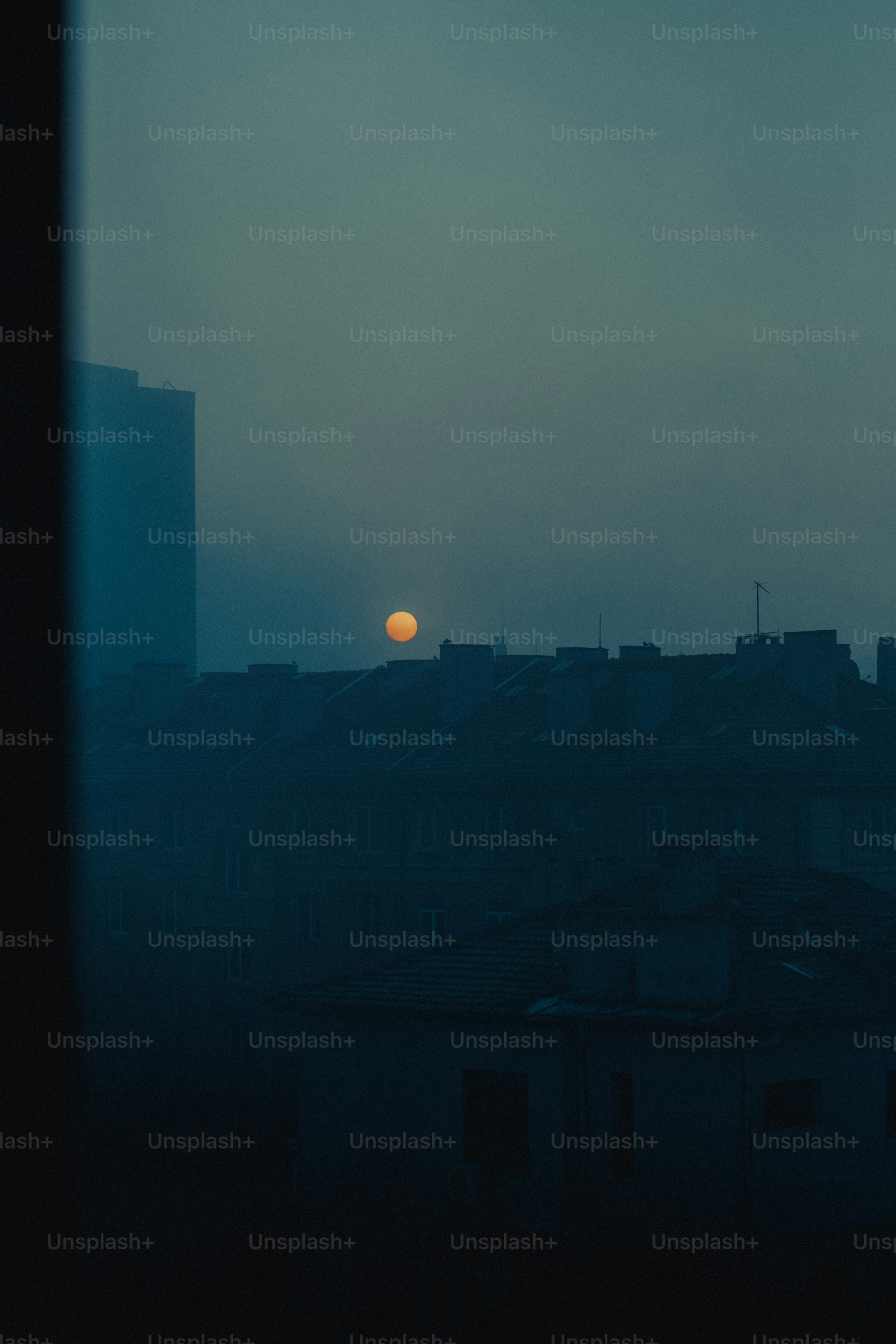 Sun setting over a hazy cityscape silhouette of city buildings.