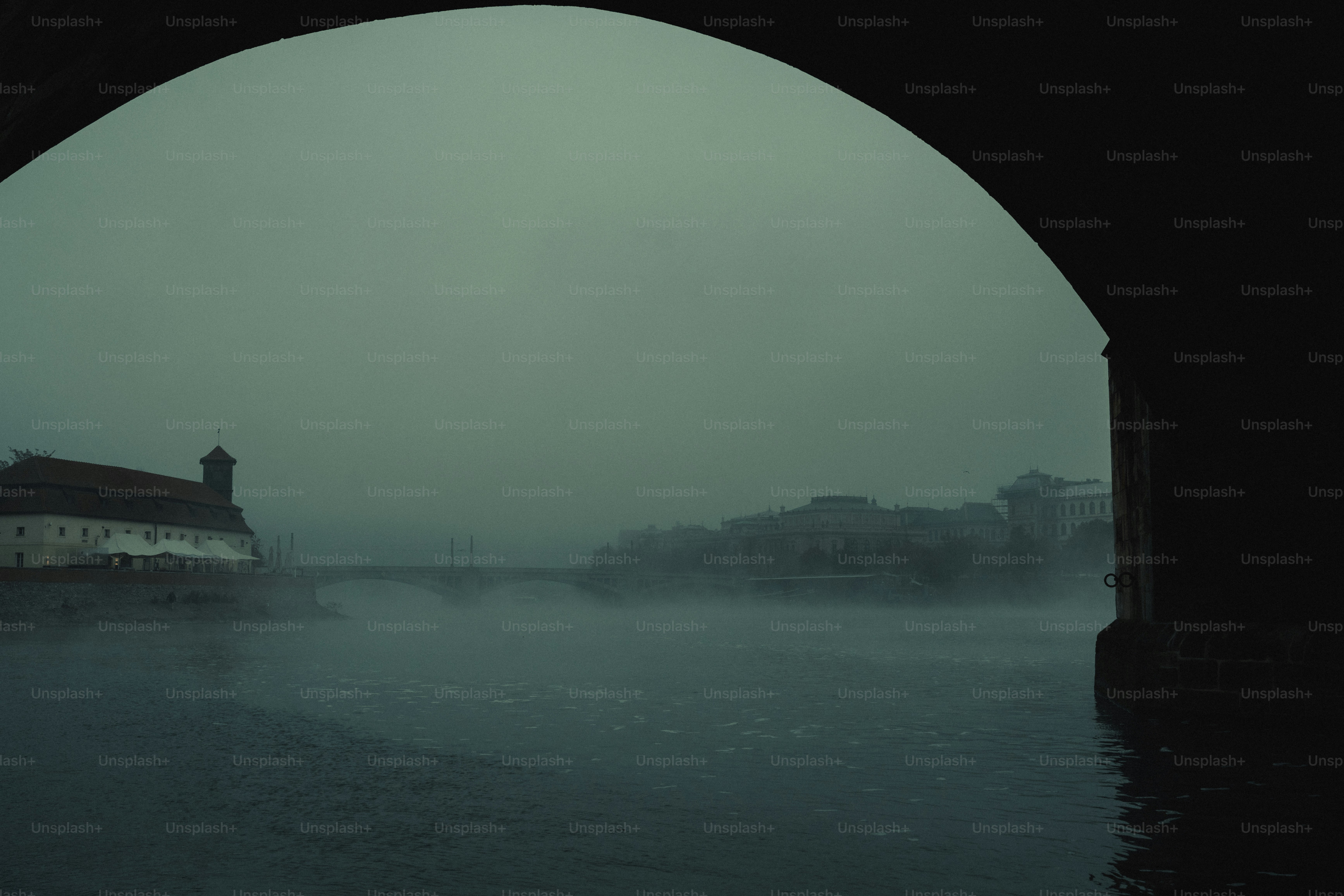 Misty river scene with old building and bridge.