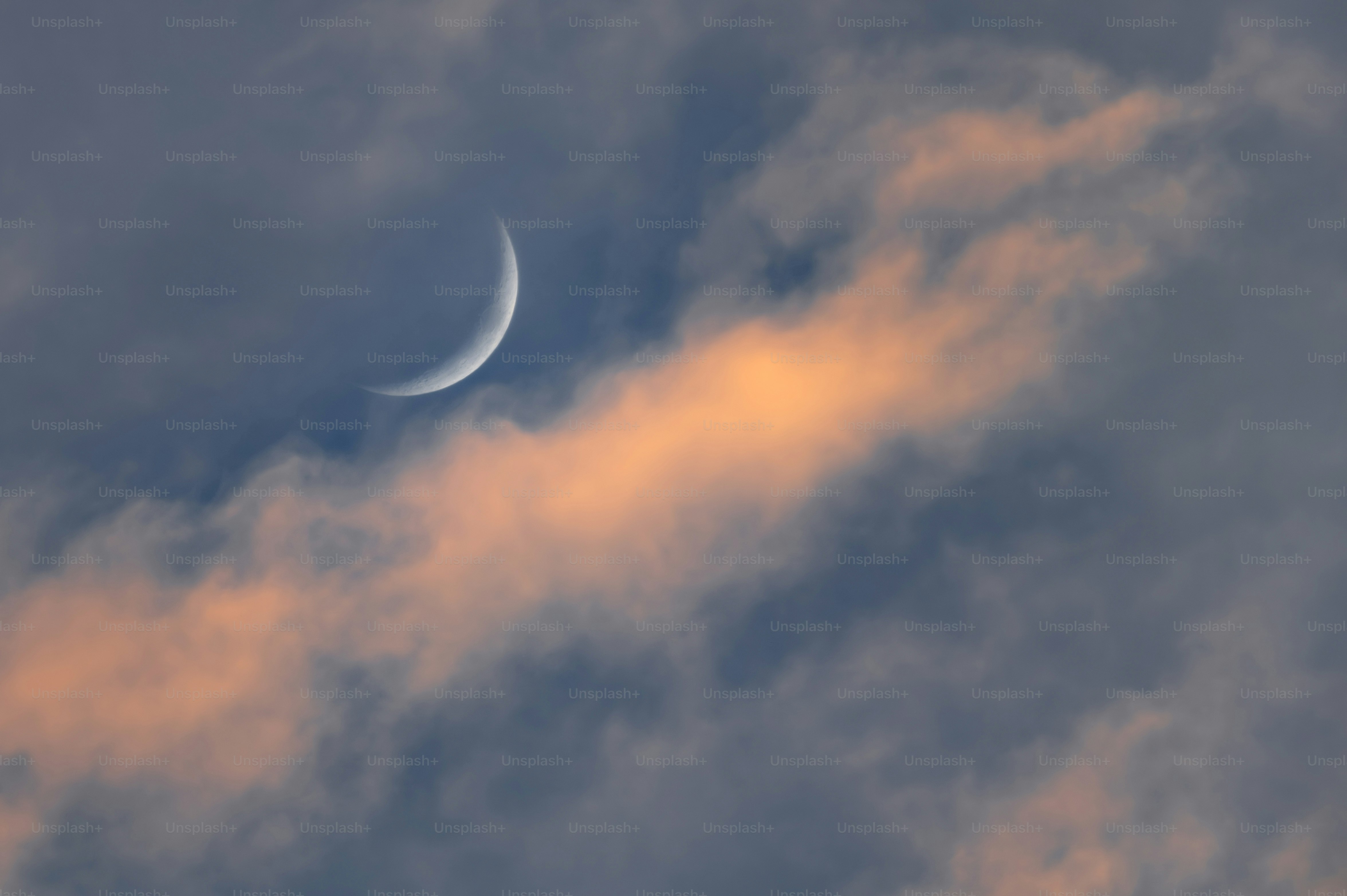 Crescent moon behind colorful clouds at dusk