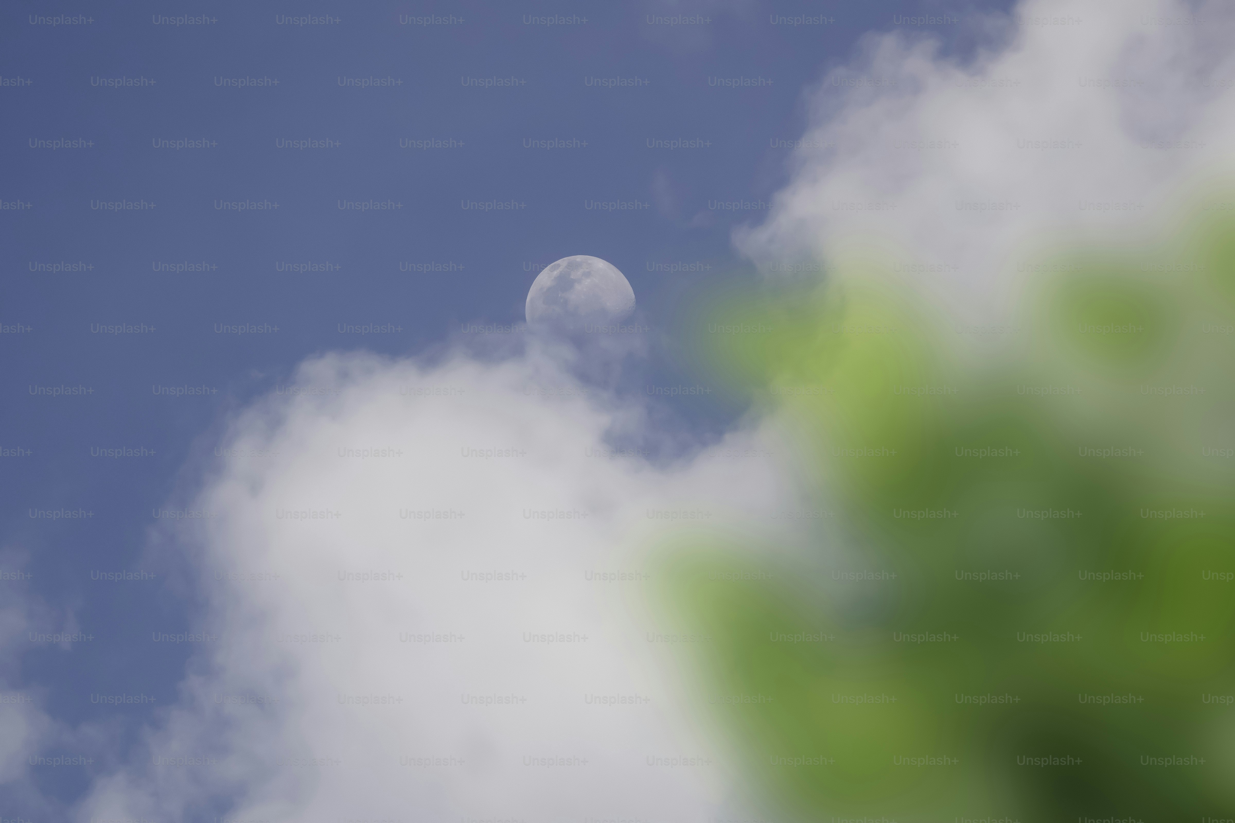 The moon peeks through clouds in a blue sky.