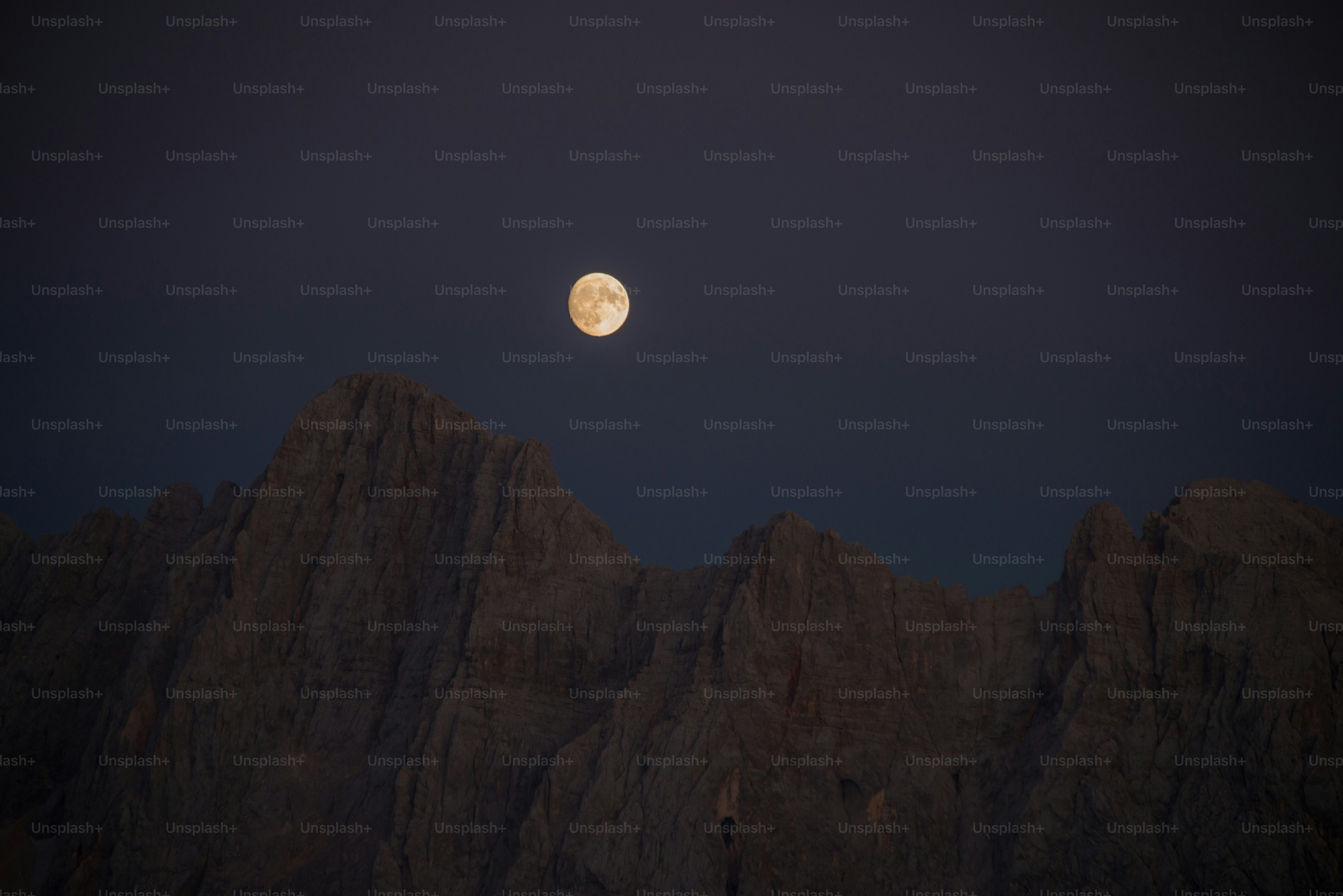 Full moon over jagged mountain peaks at dusk.