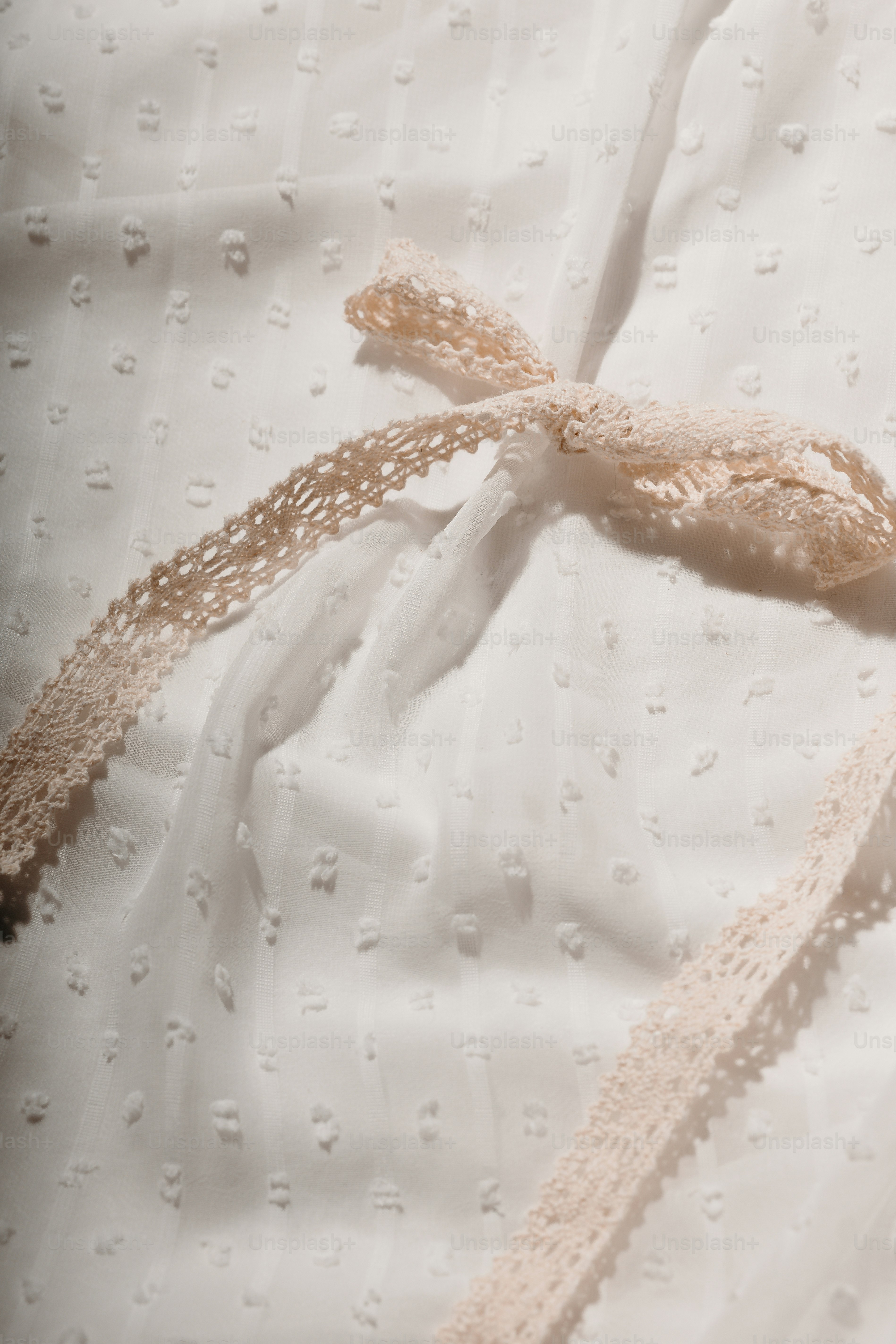 Un ruban délicat en dentelle noué sur un tissu blanc.