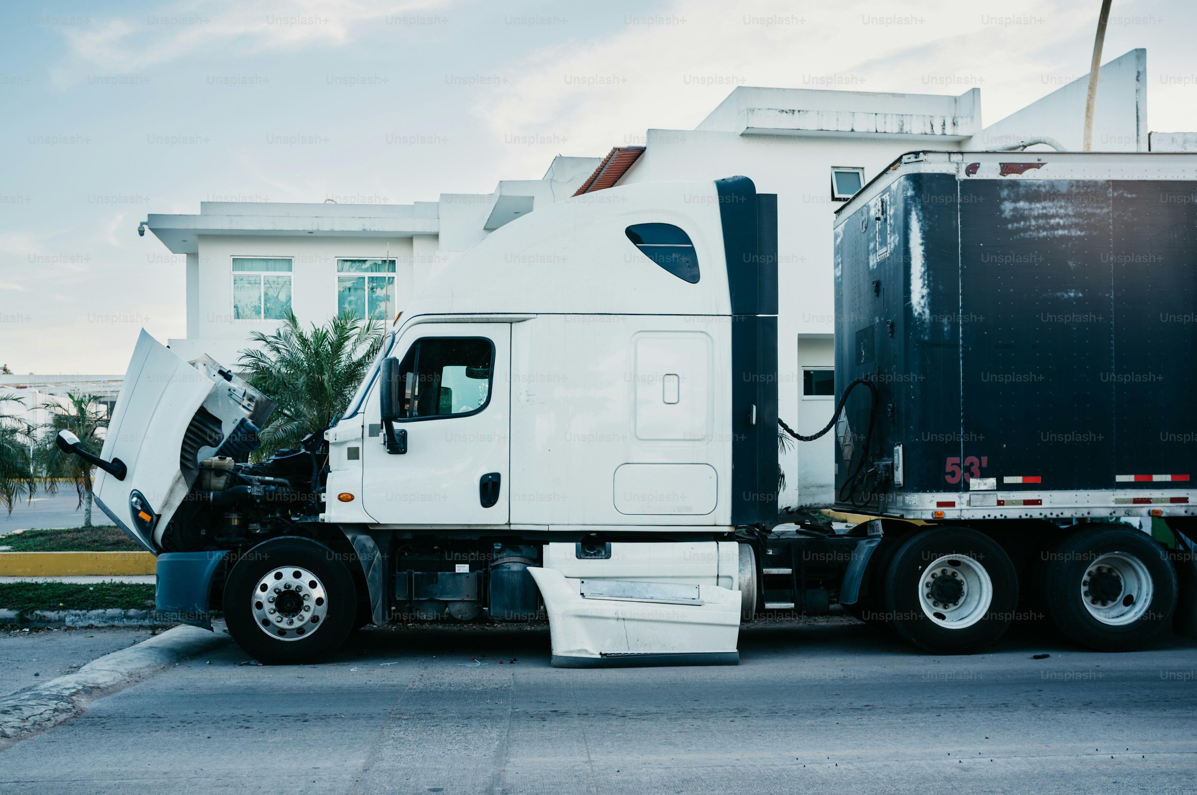 White semi-truck with hood open parked on street.