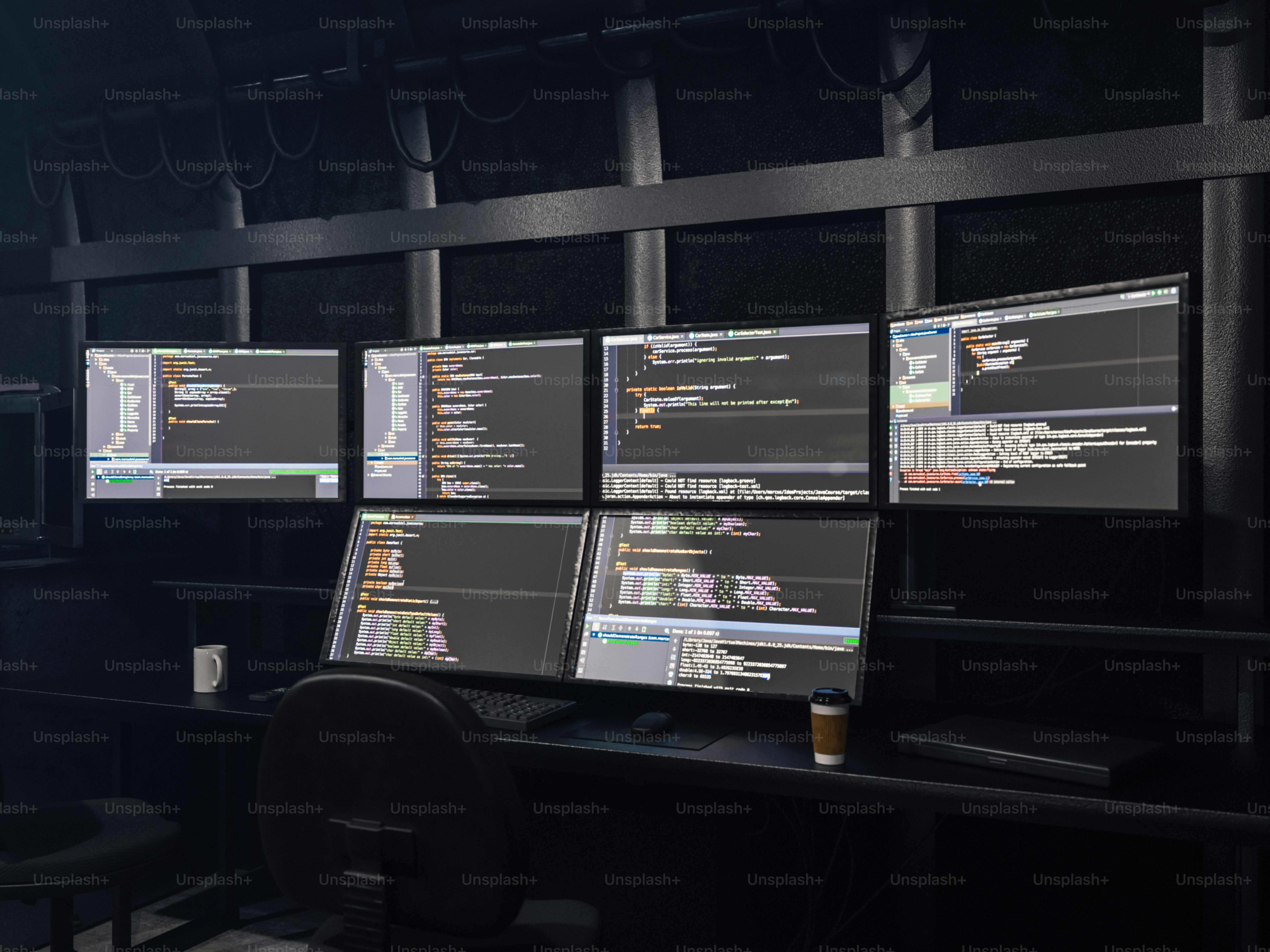 Beberapa monitor komputer menampilkan kode di ruangan gelap.
