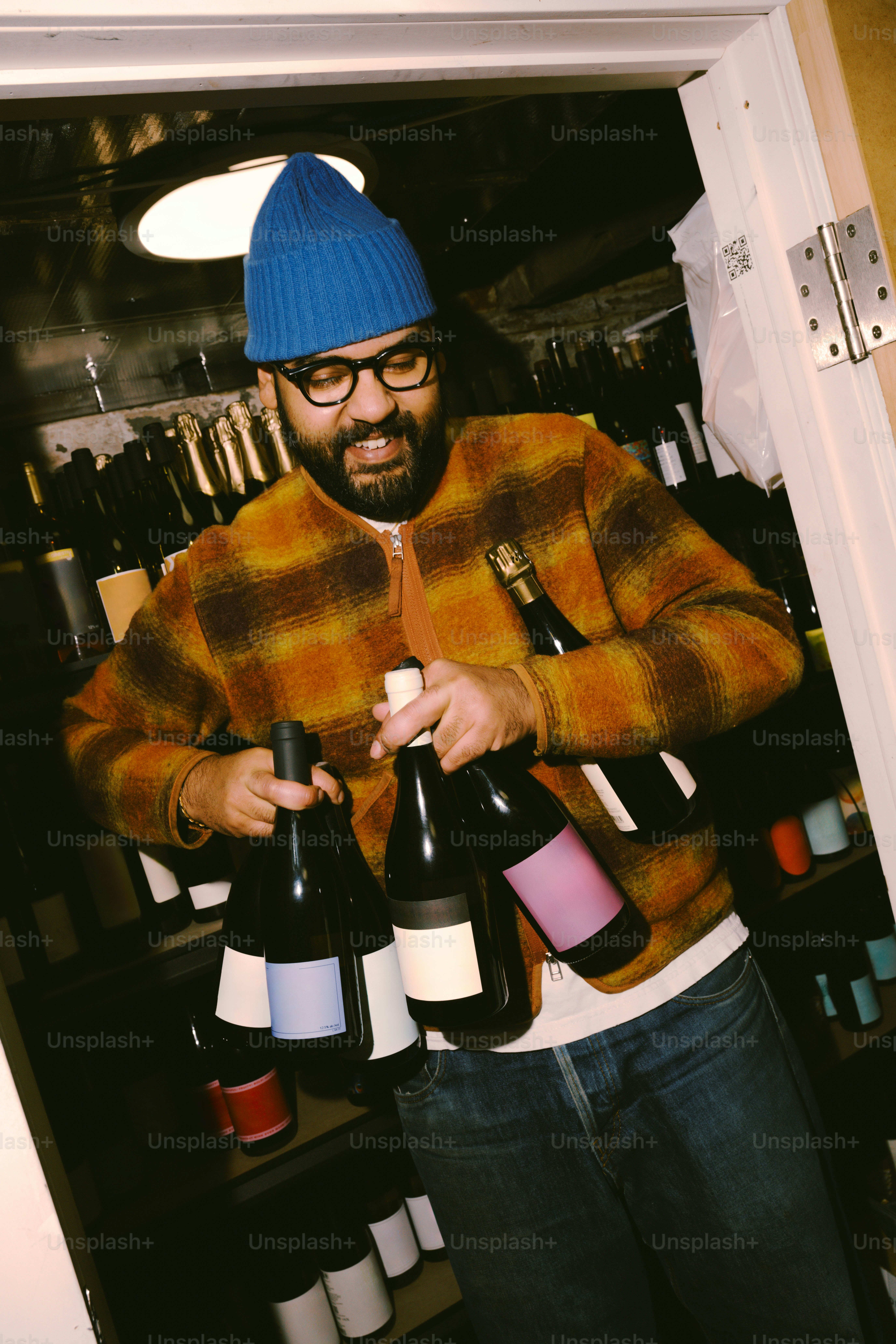 Man in blue hat carries several wine bottles