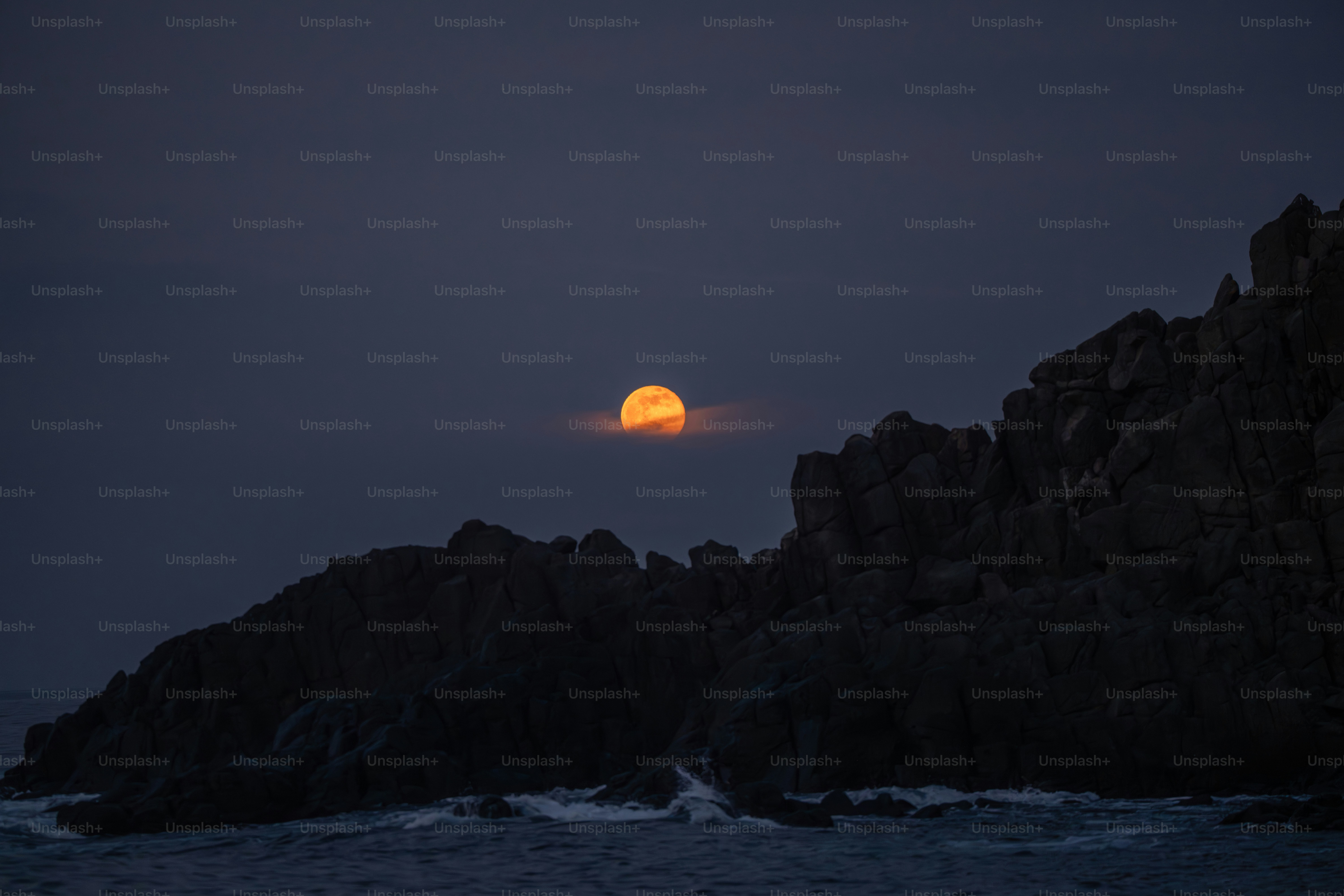 Full moon rising over rocky coastline at dusk