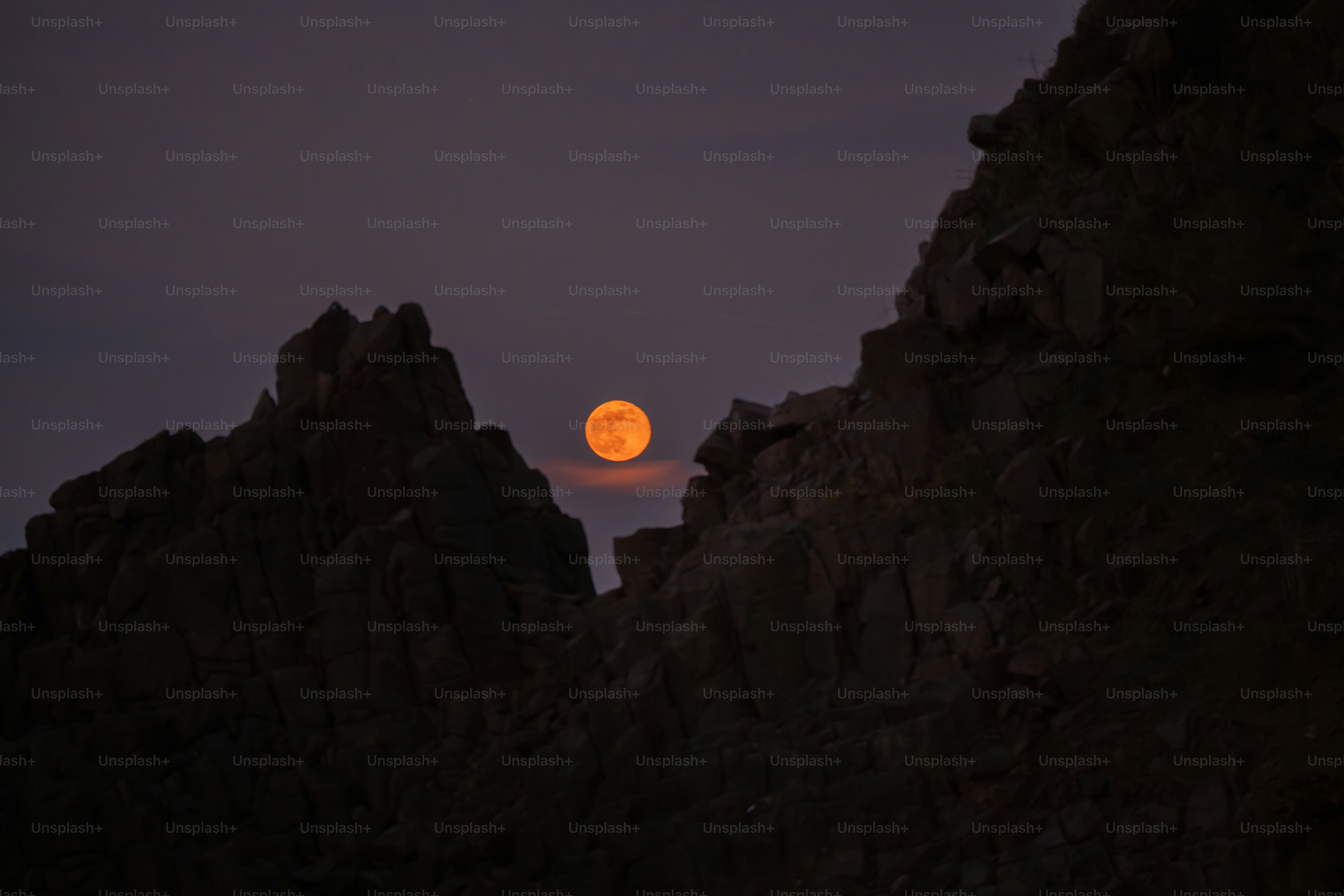 황혼 무렵 바위산 봉우리 사이로 떠오르는 주황색 달