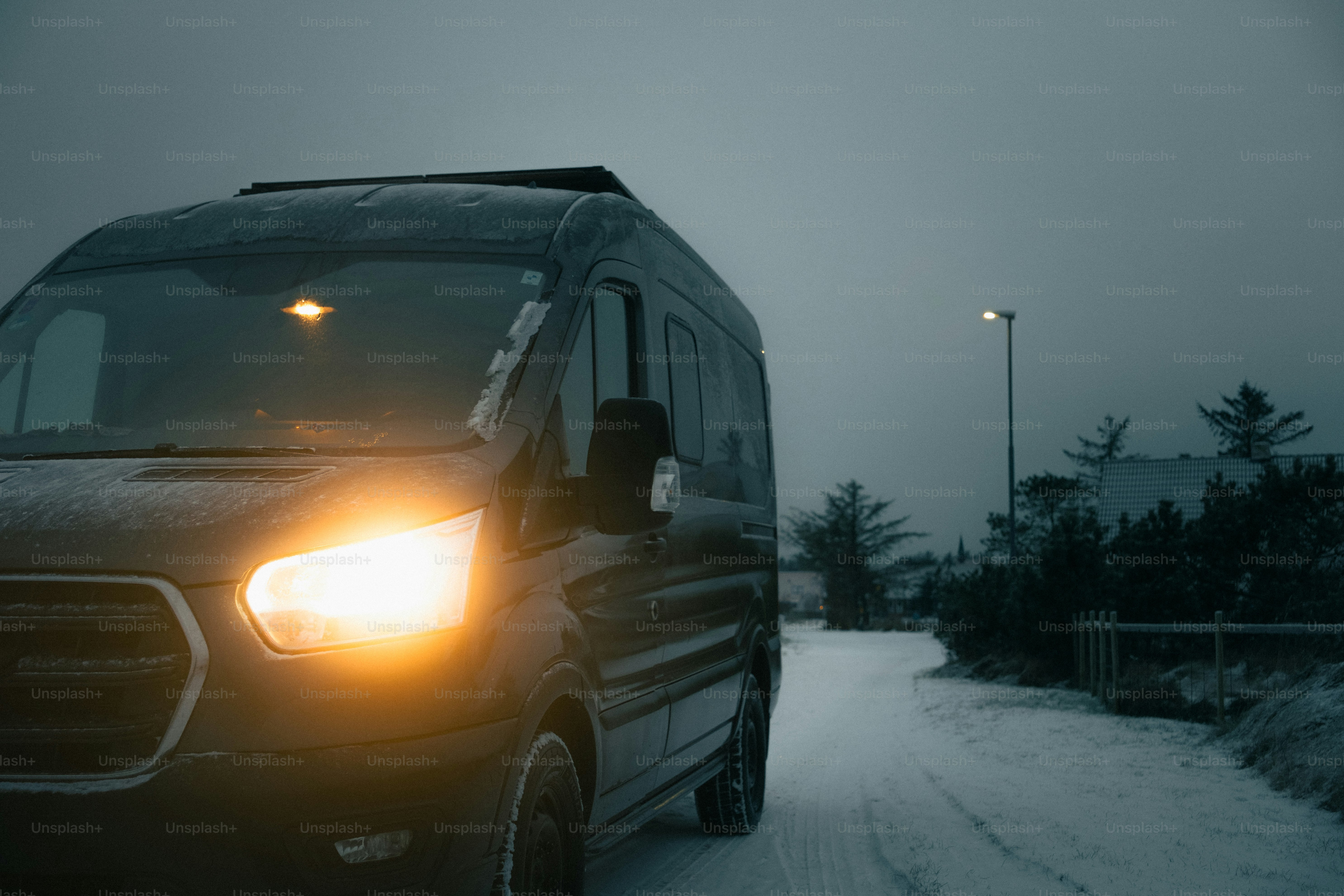 A dark van driving on a snowy road at dusk.