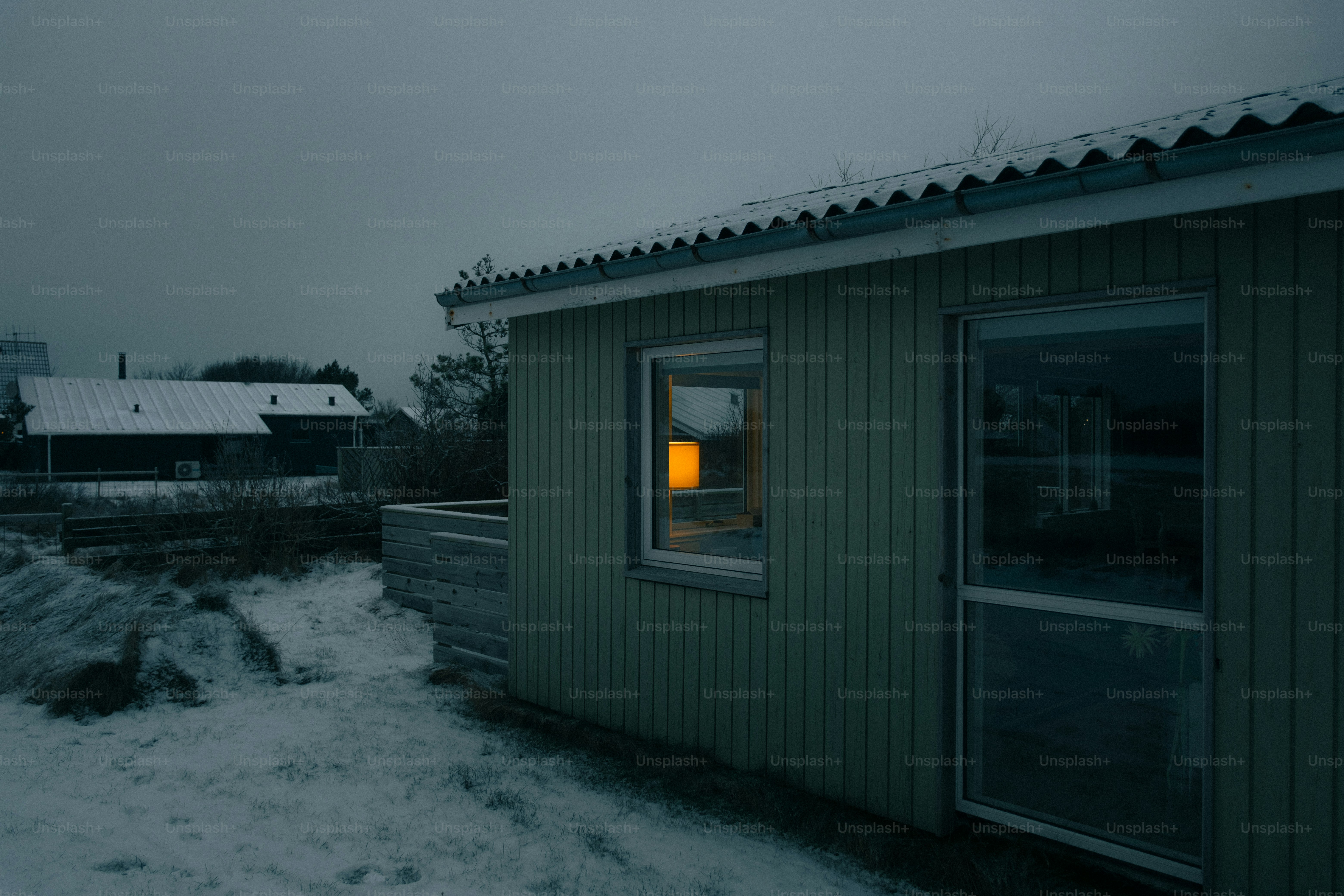 Small house with glowing window in snowy landscape.