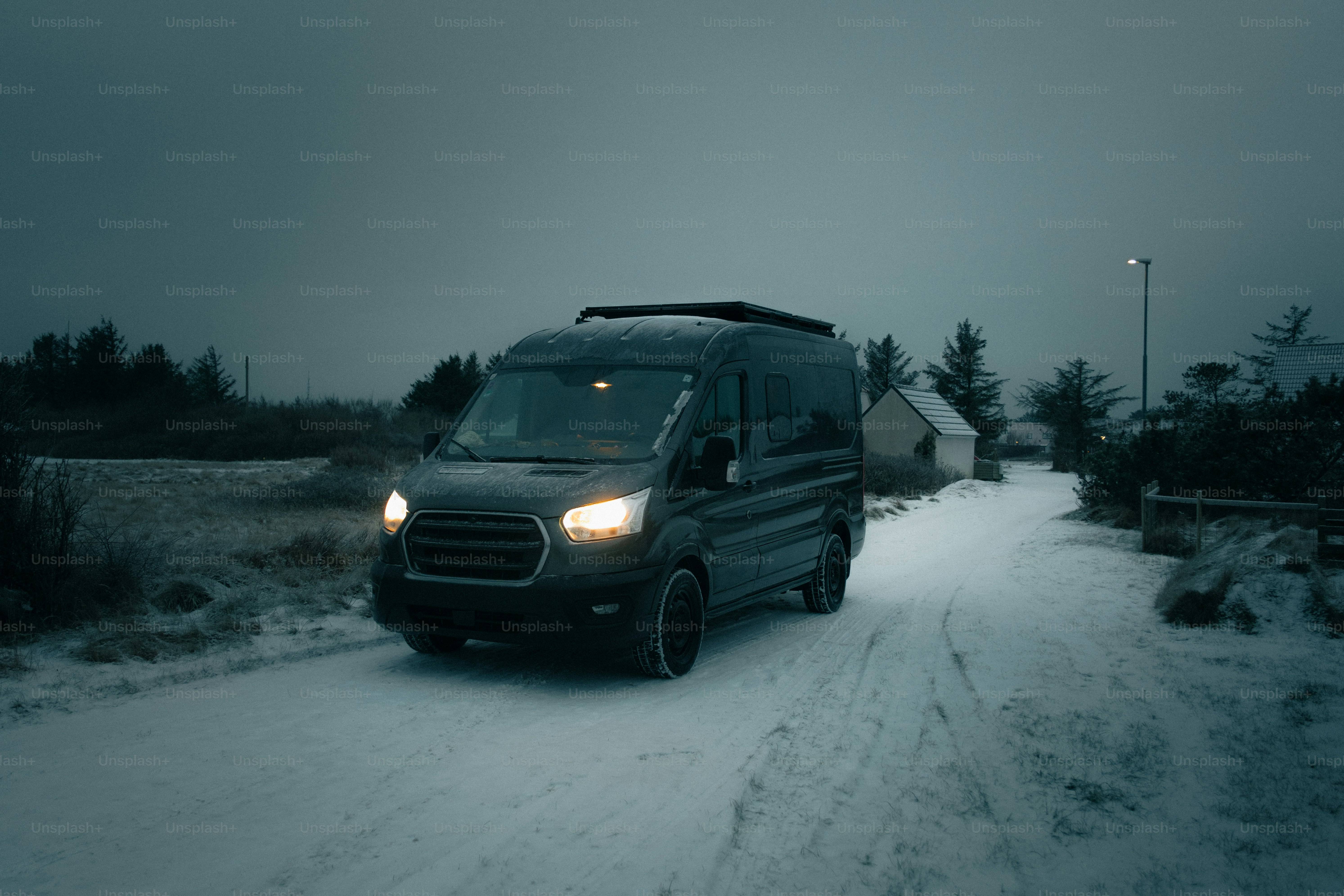 A dark van drives down a snowy road at dusk.