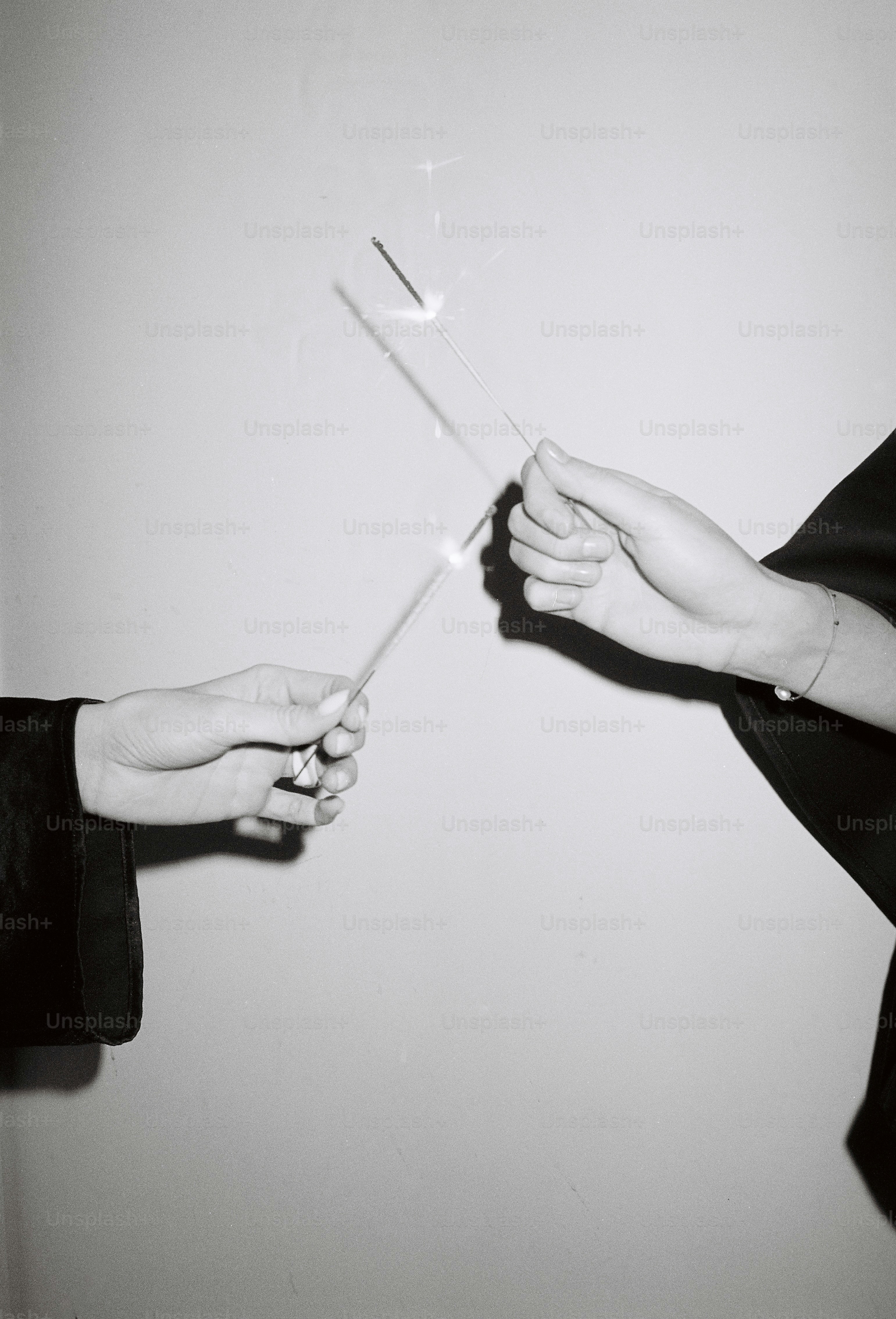 Two hands holding sparklers against a plain background
