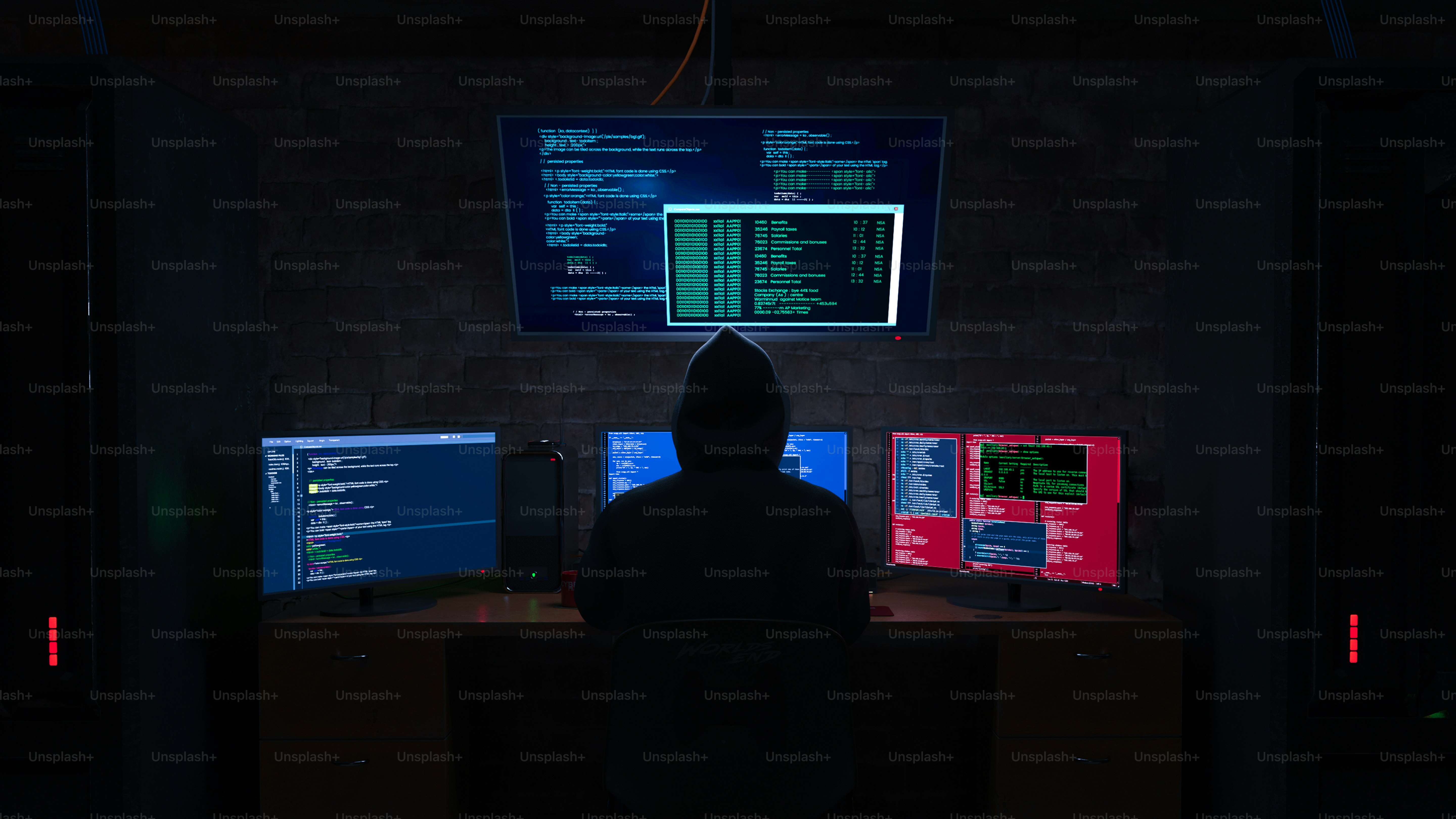 Hacker in a dark room surrounded by computer monitors.