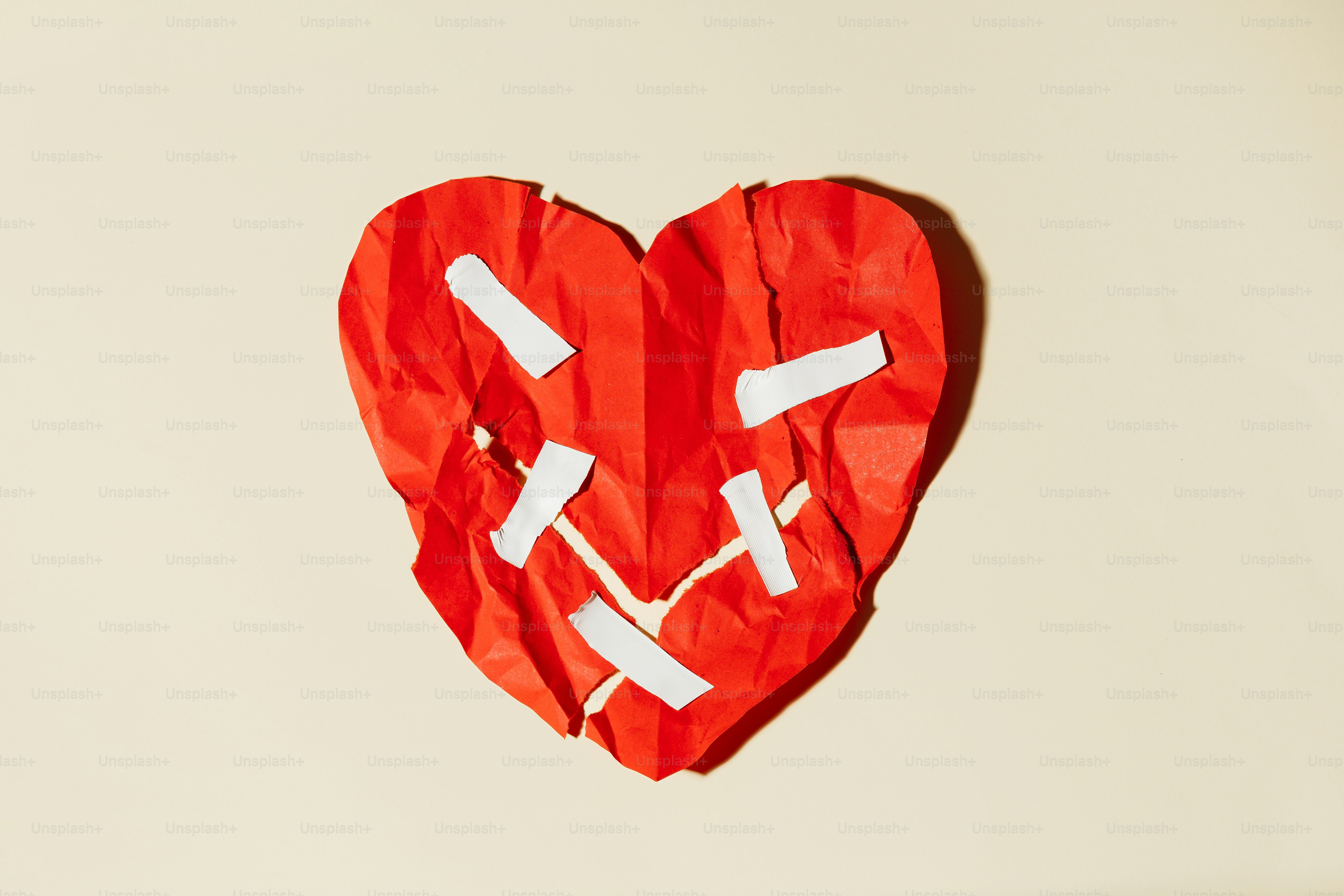 Crumbled red heart taped together on a plain background