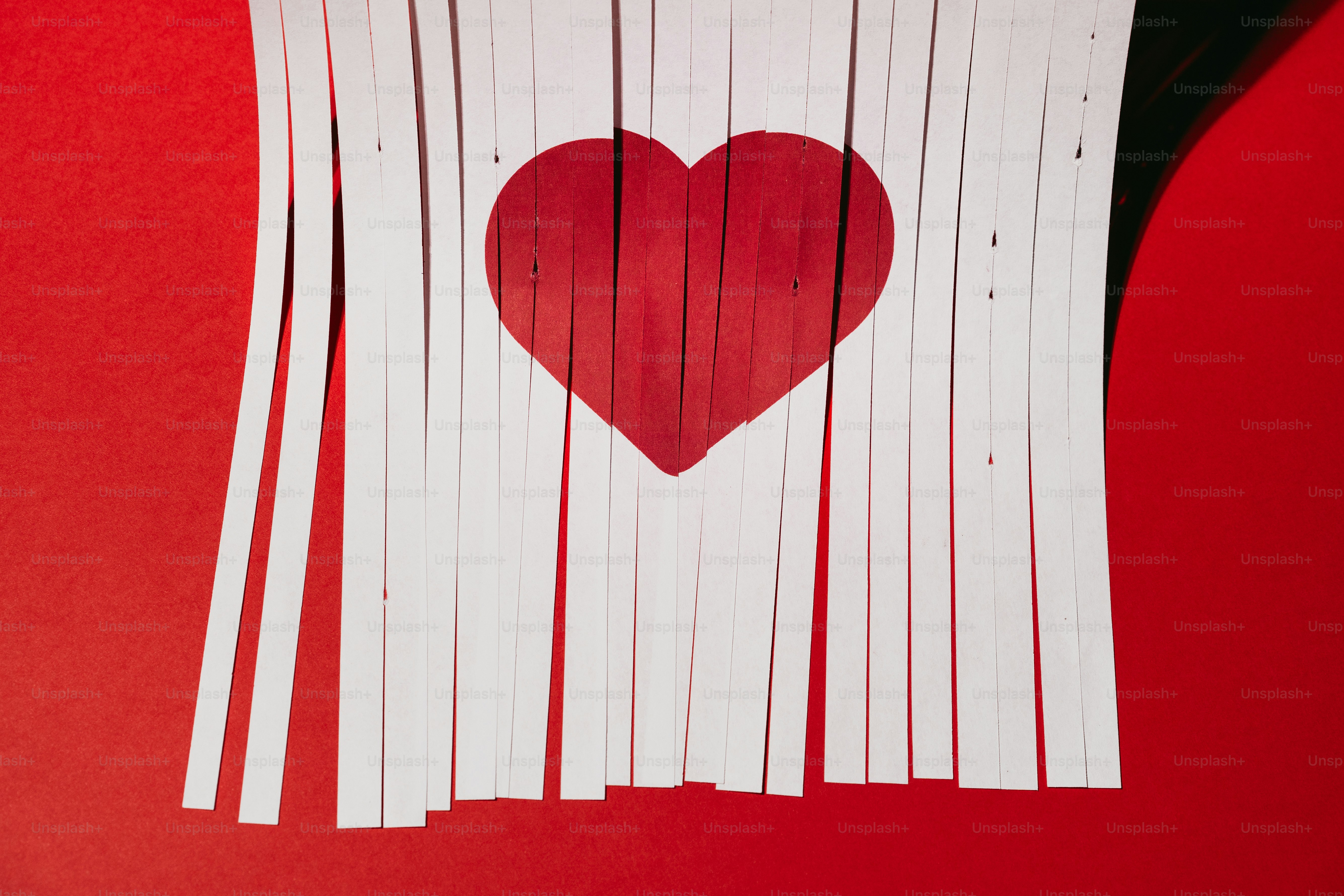 A red heart shape behind torn white paper.