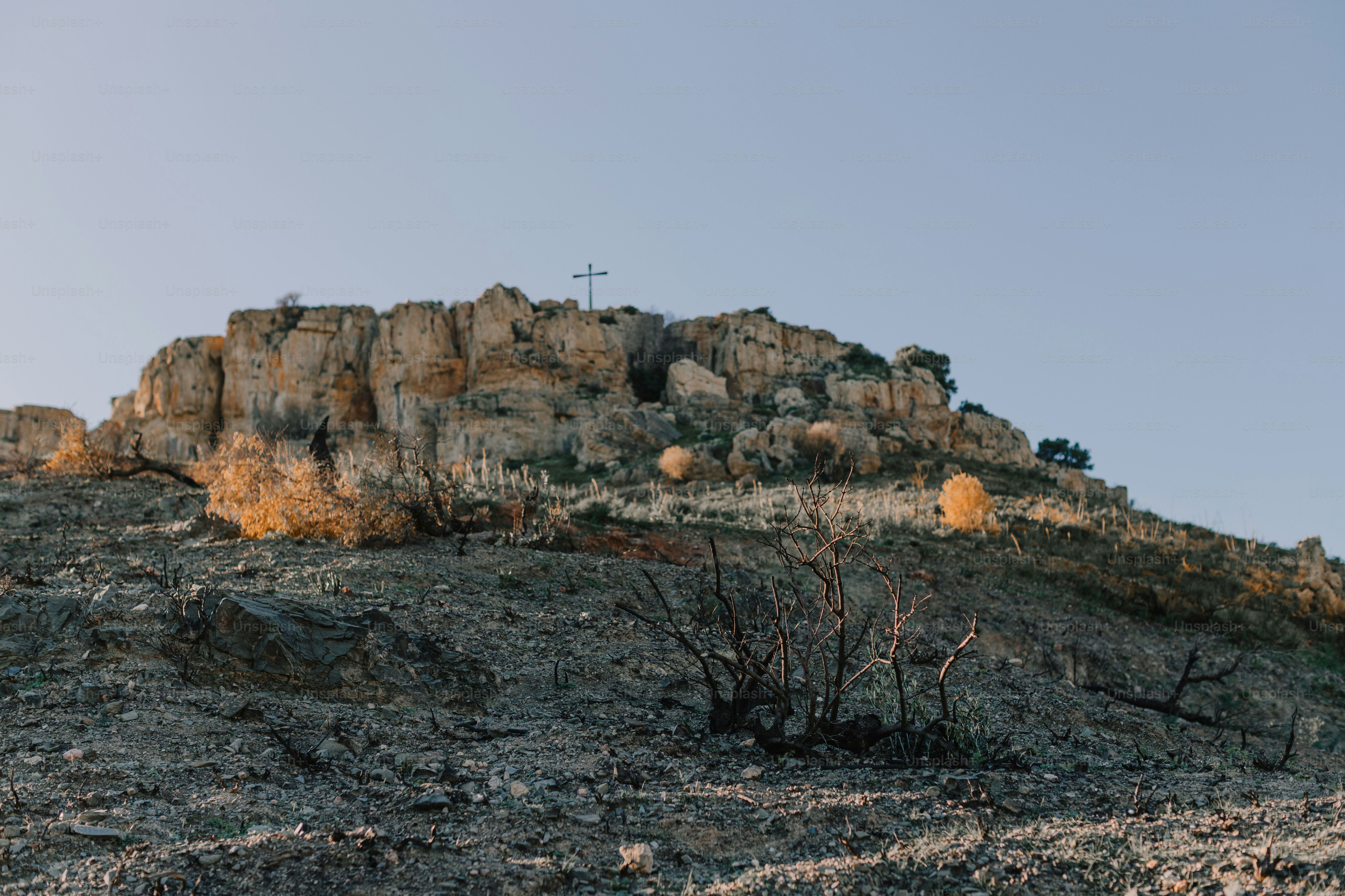 Rocky hill with a cross on top at sunset