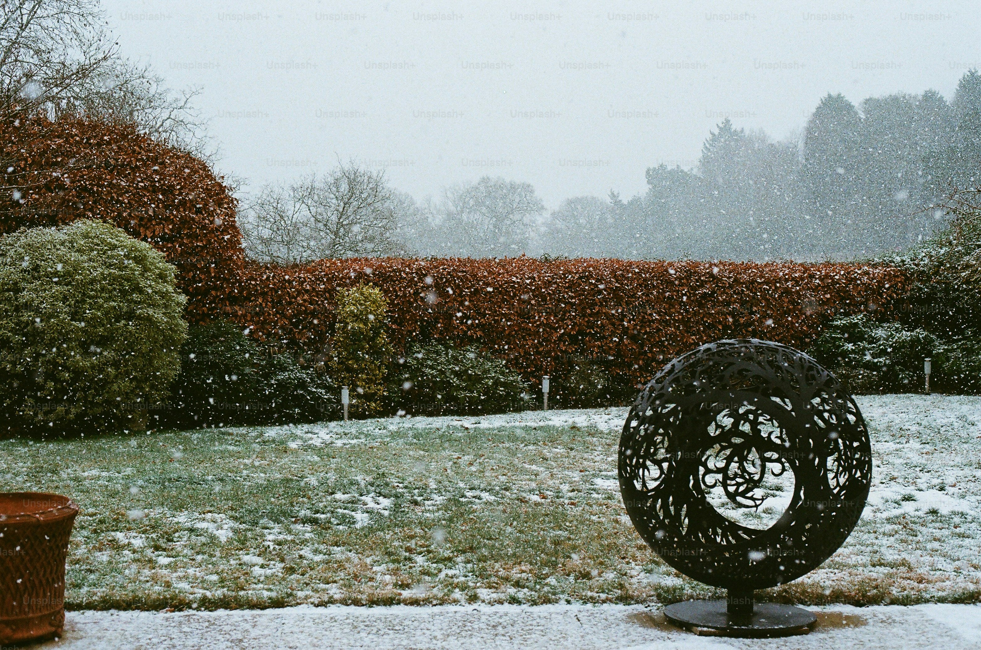 A garden scene with falling snow and decorative orb.