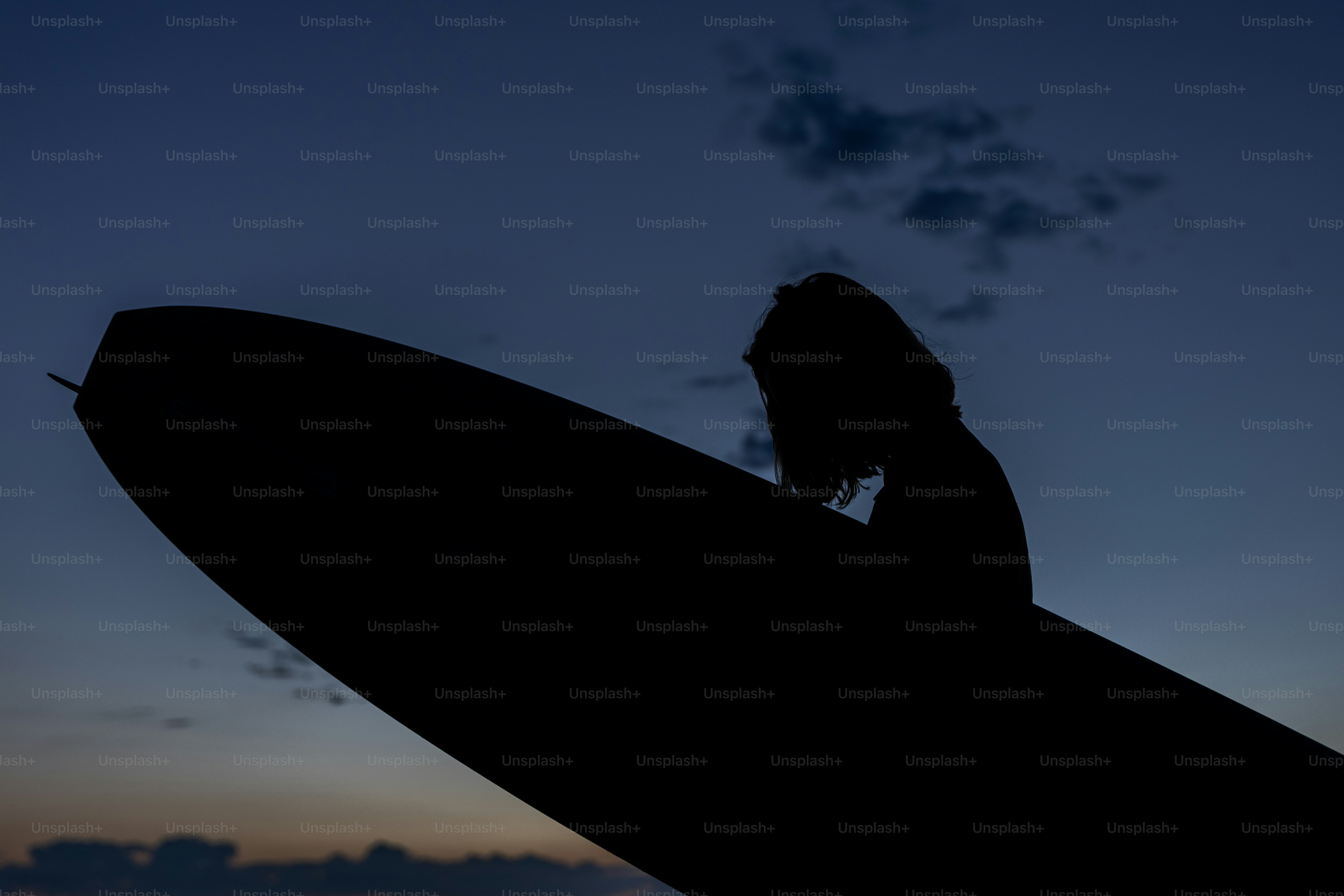 Silhouette d’un surfeur avec une planche de surf contre le ciel du crépuscule