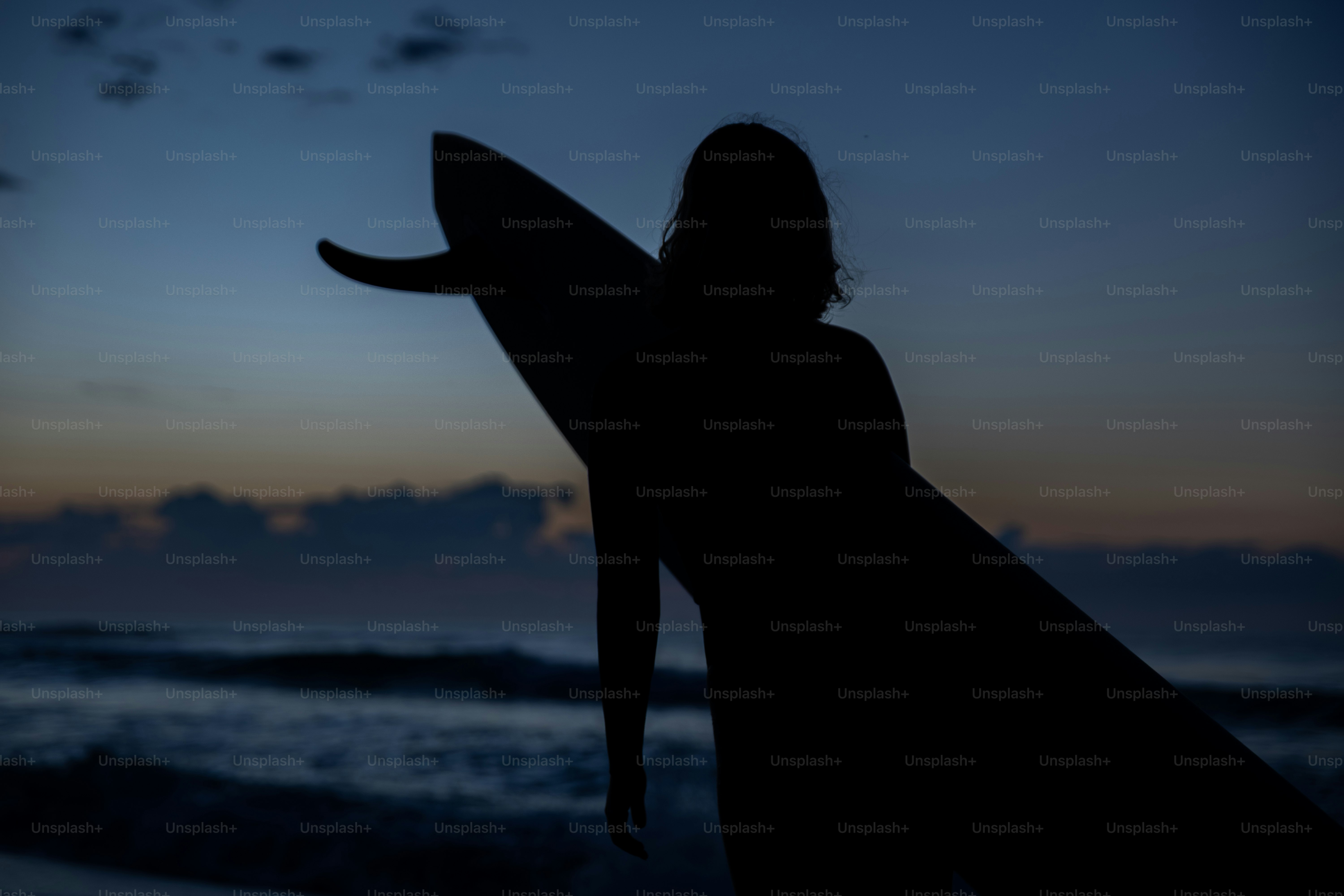 Silhouette di un surfista che tiene una tavola da surf al crepuscolo.