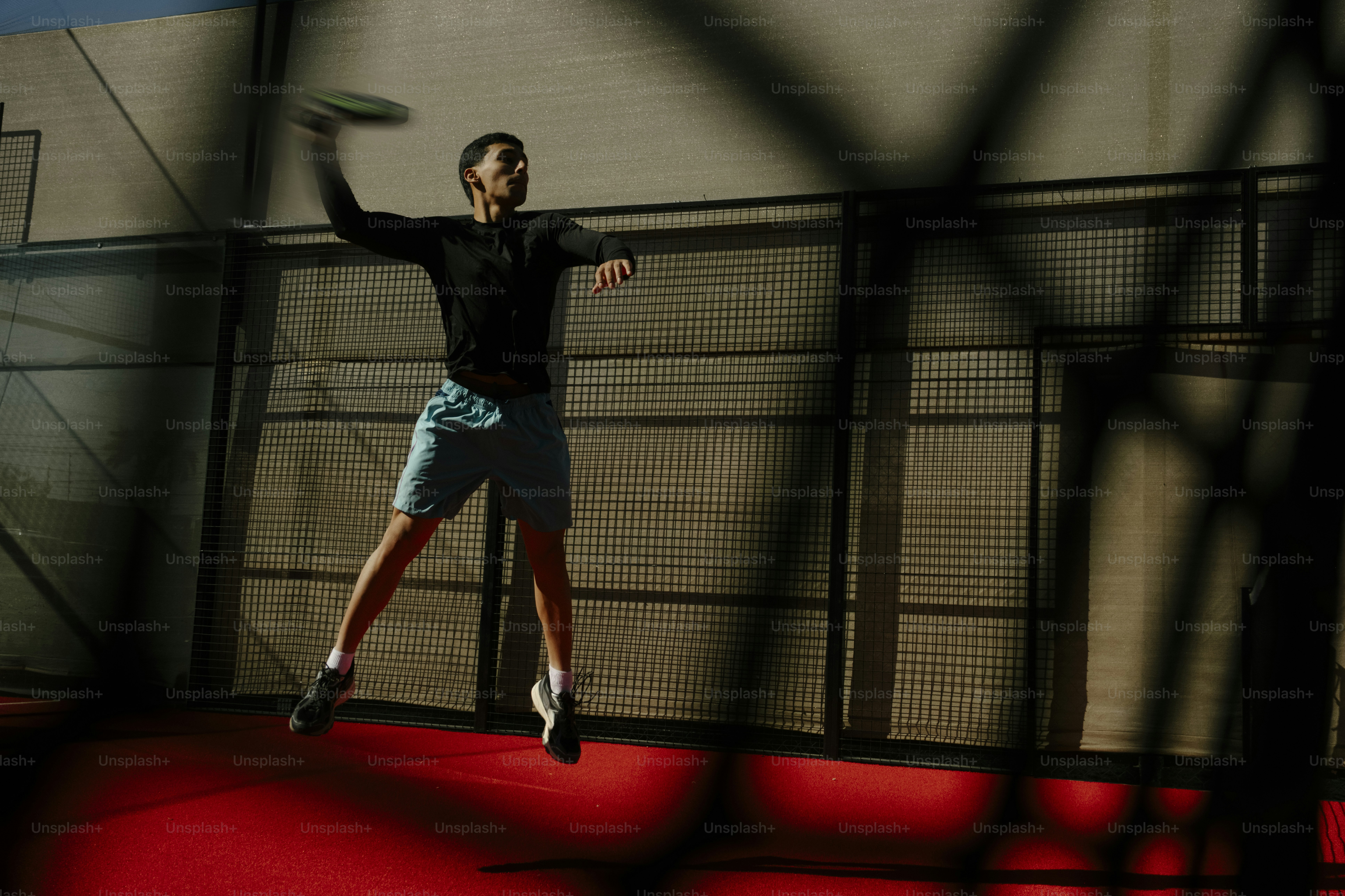 赤いコートでパデルテニスをしている男。