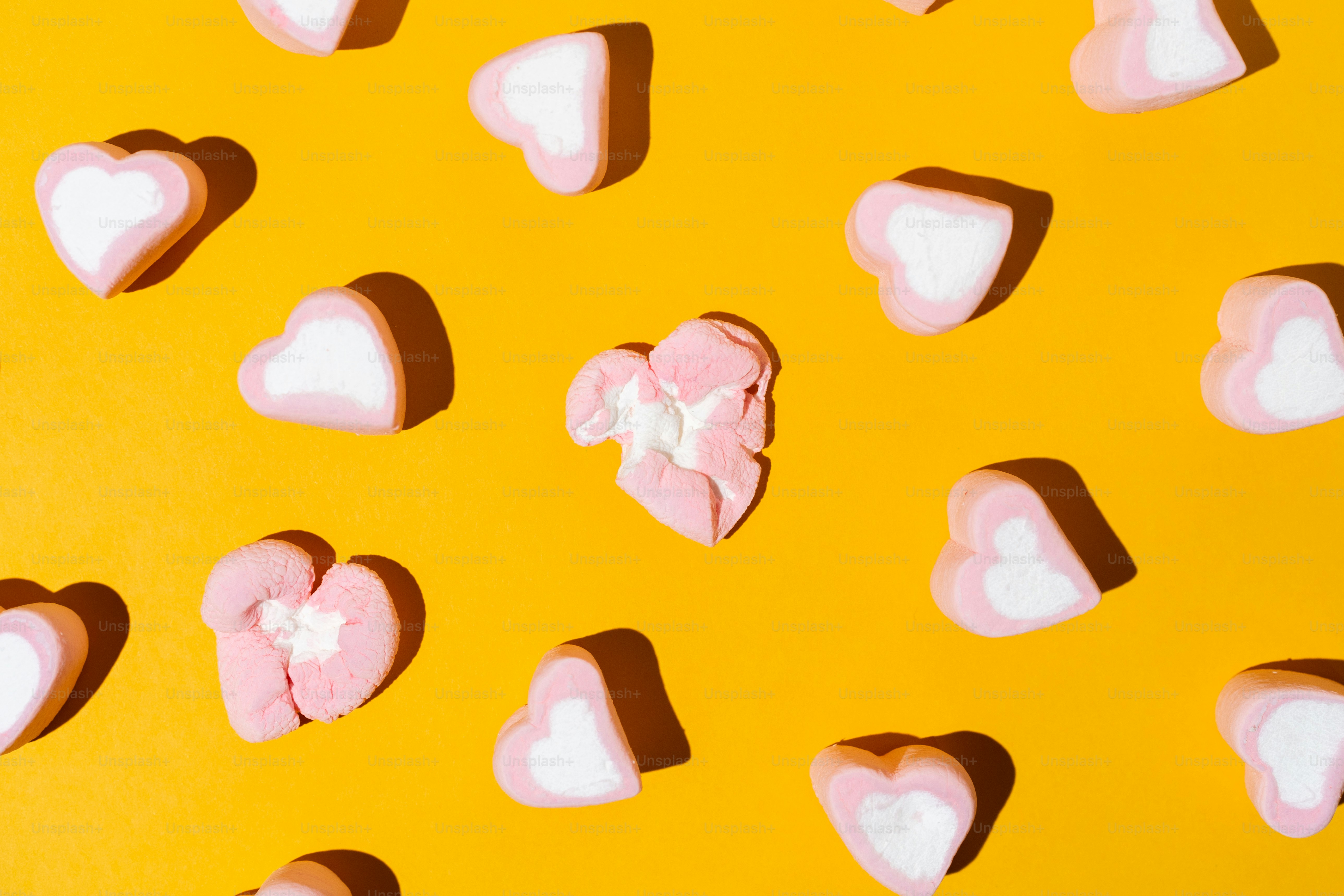 Herzförmige Marshmallows, verstreut auf gelbem Hintergrund.