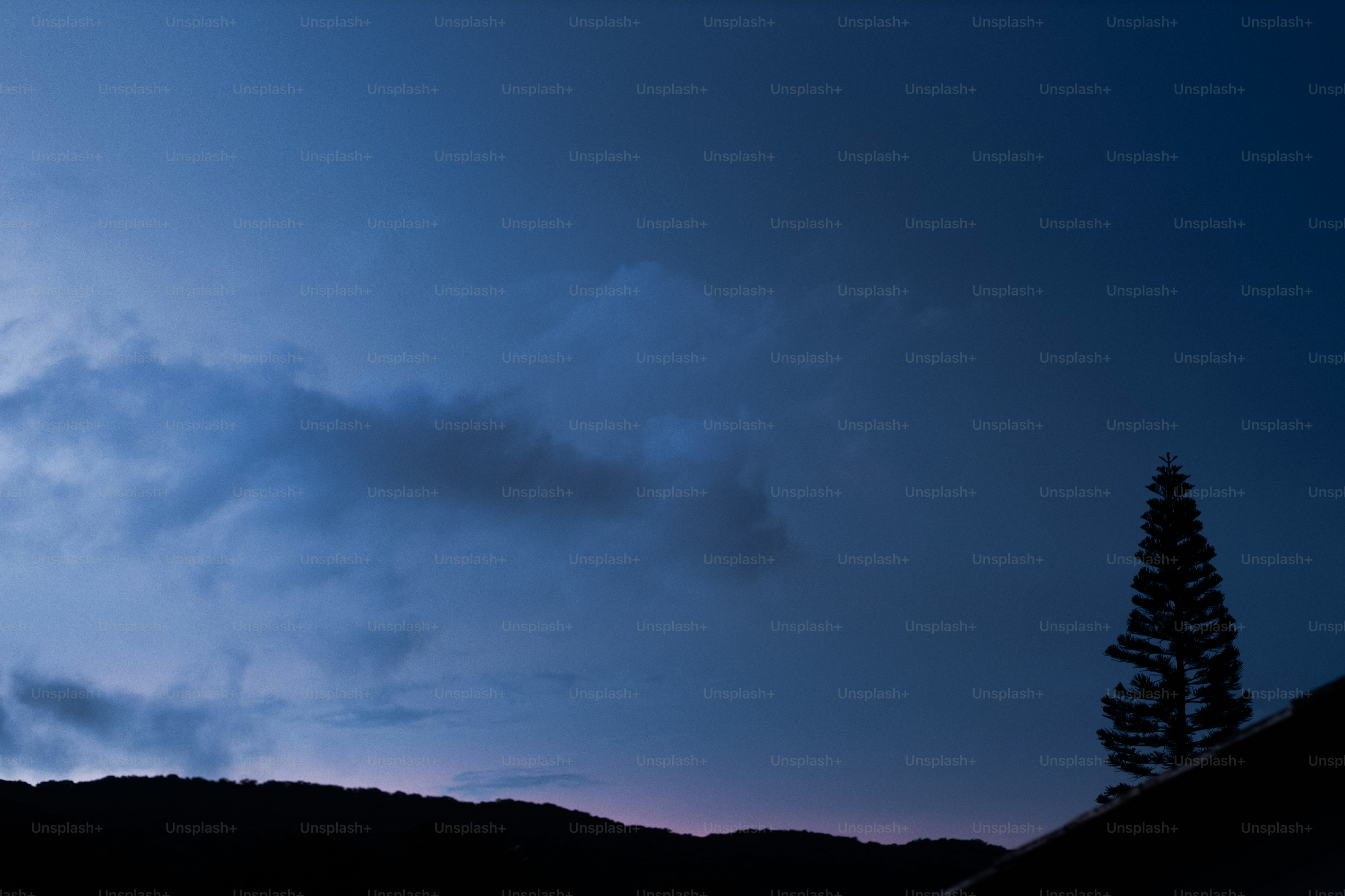 Dark blue sky with clouds over silhouetted landscape.