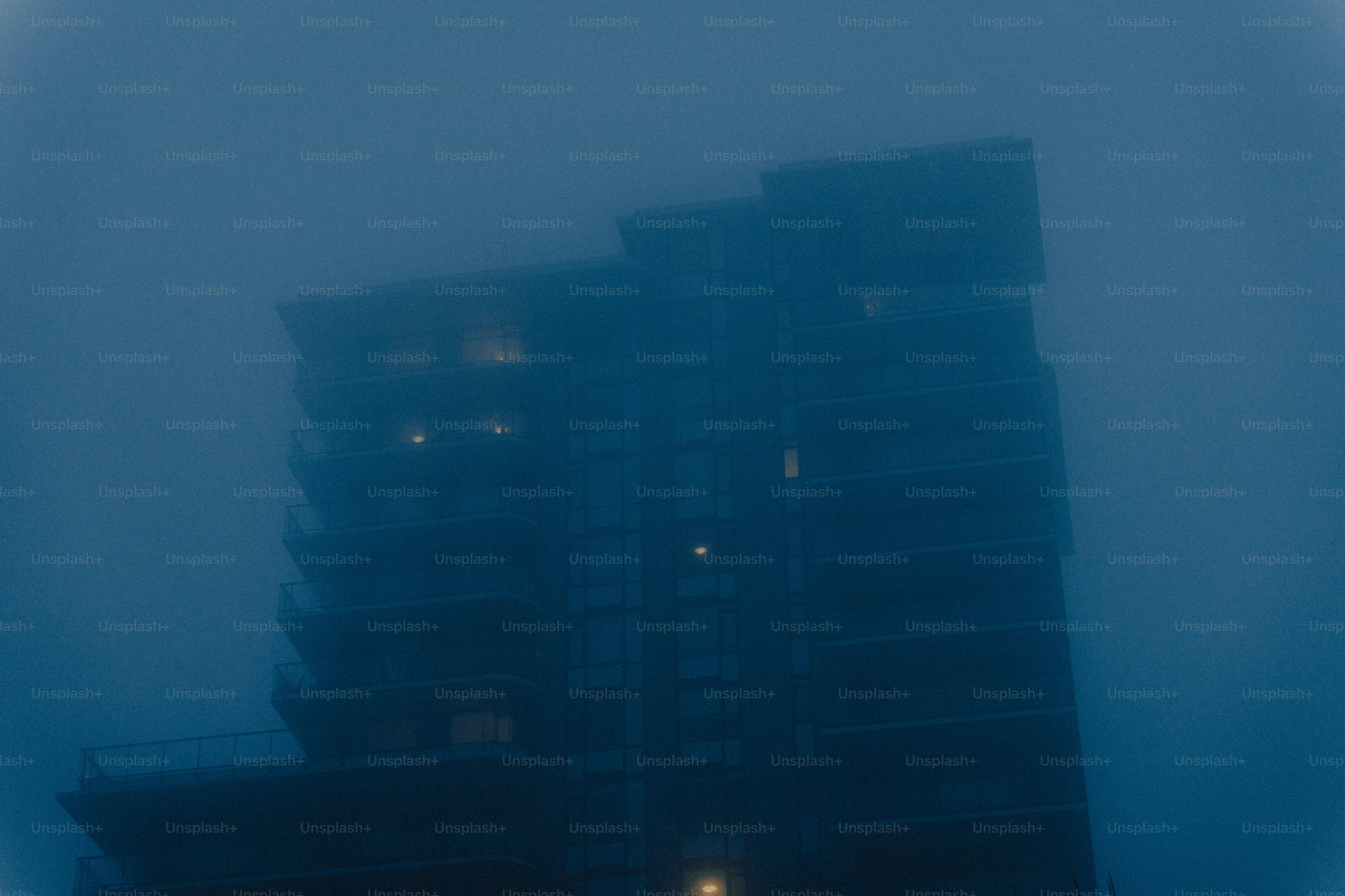 A dark building emerges from dense blue fog.