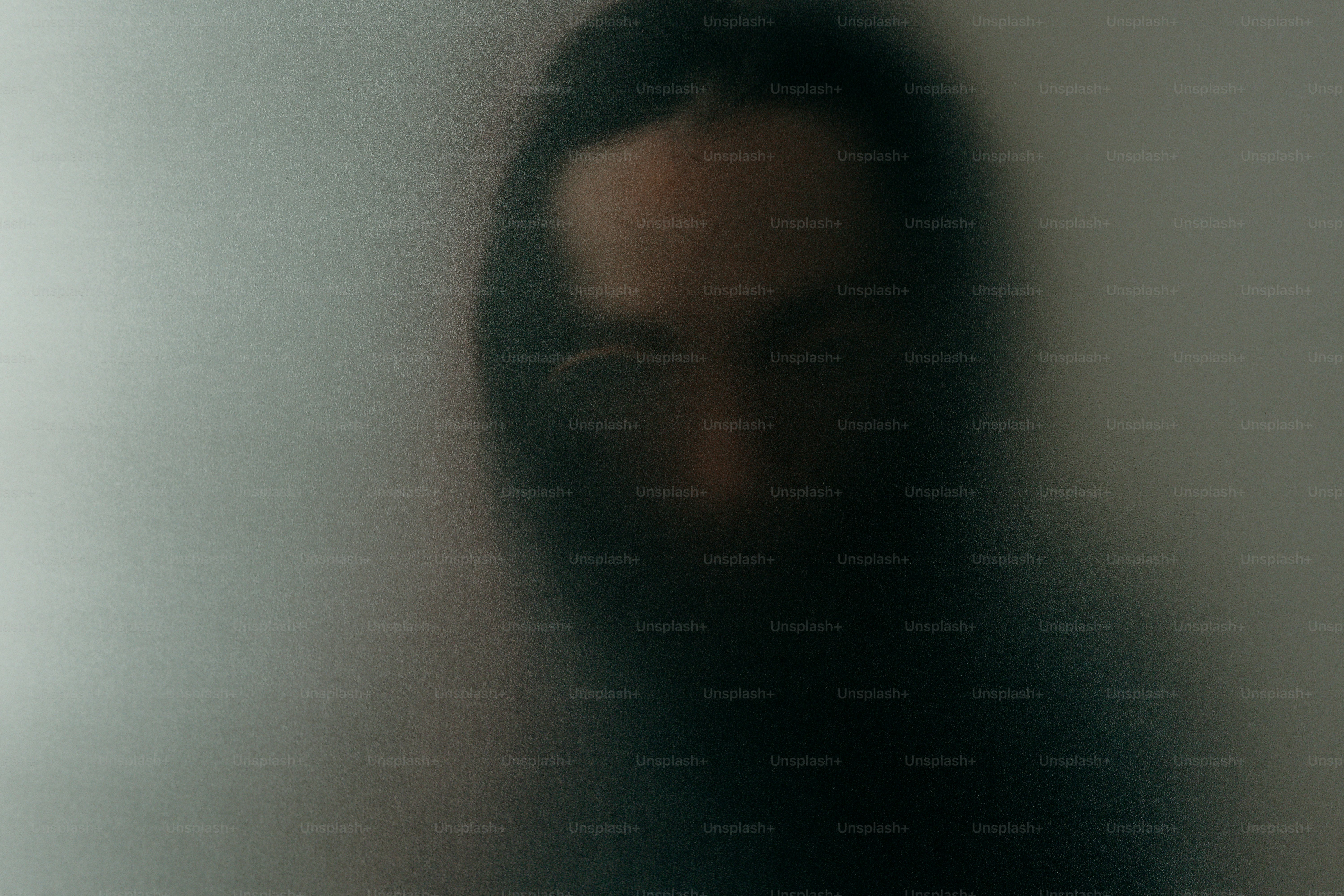 Blurred face of a person behind frosted glass.