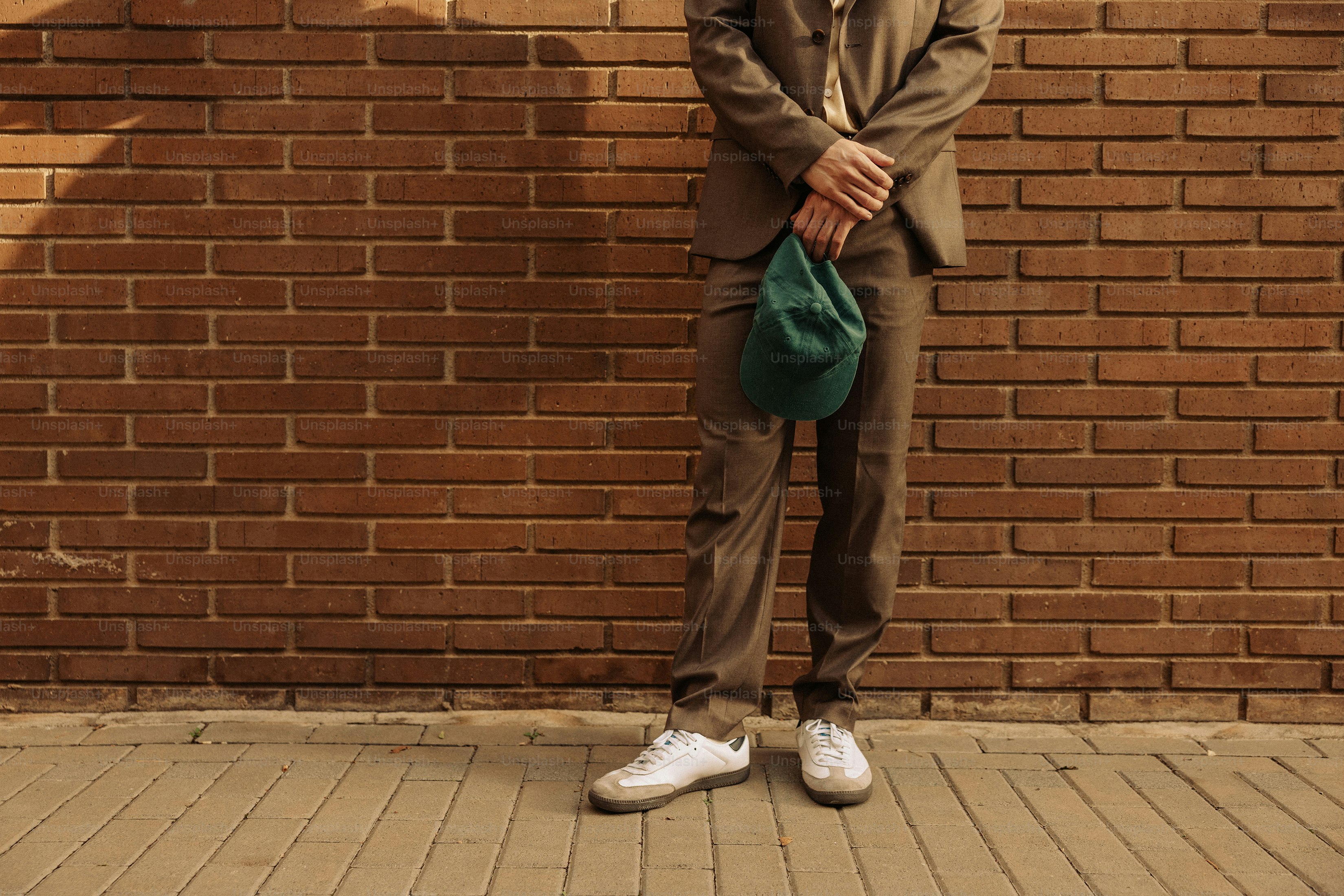 Man in suit holding cap against brick wall