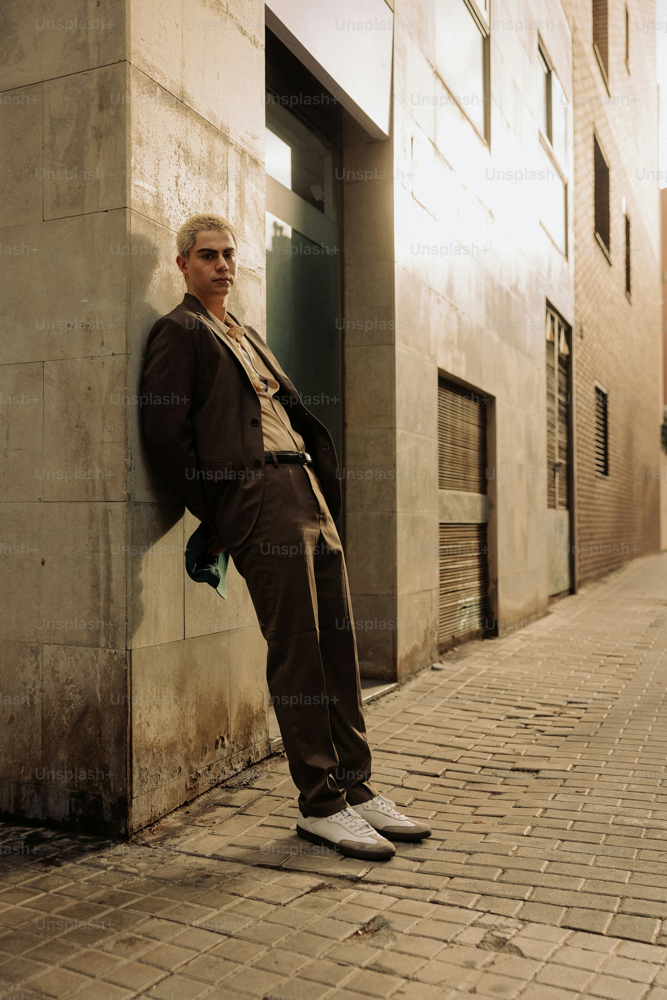 Man in a suit leans against a building wall.