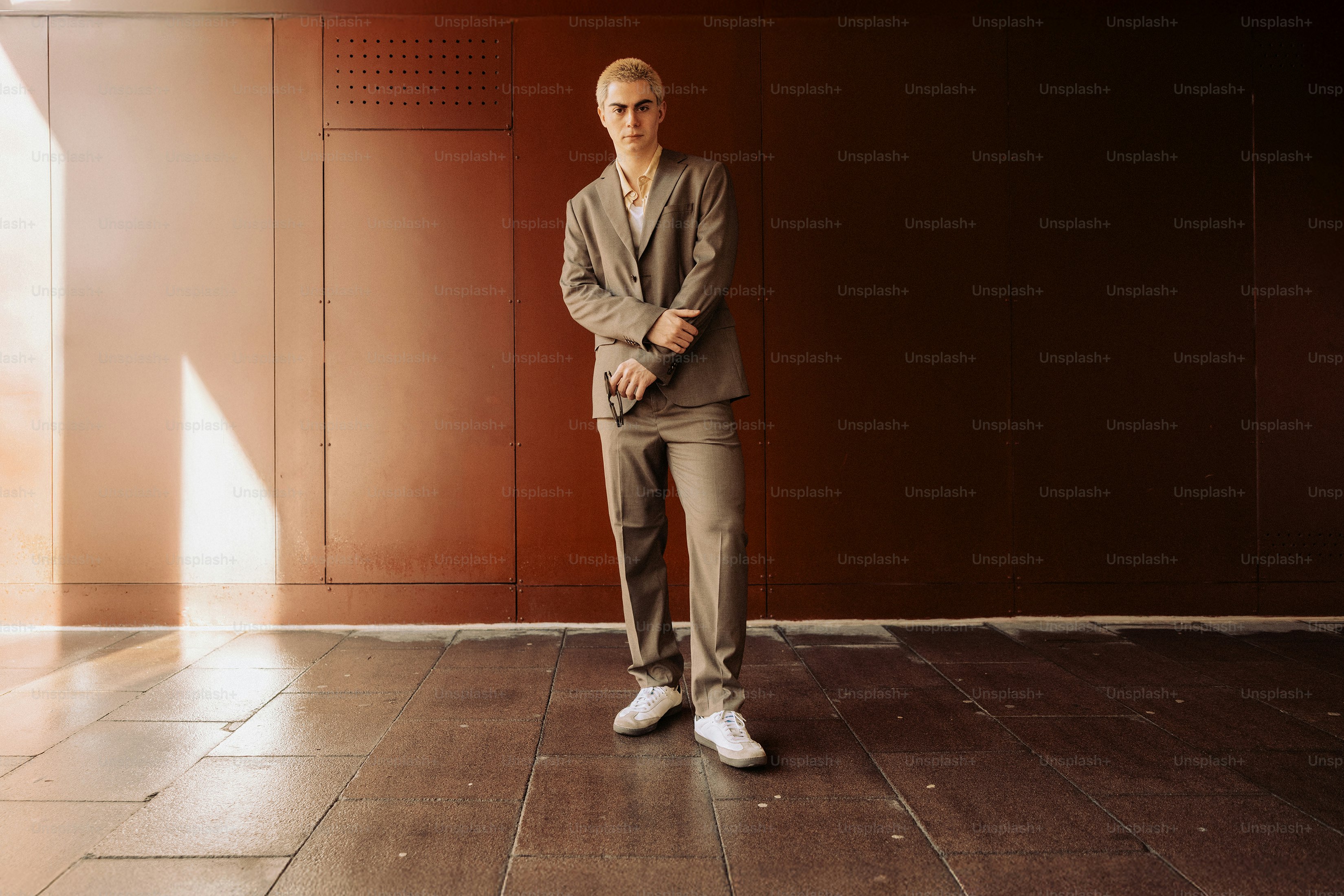 Young man in a suit stands against a brown wall.