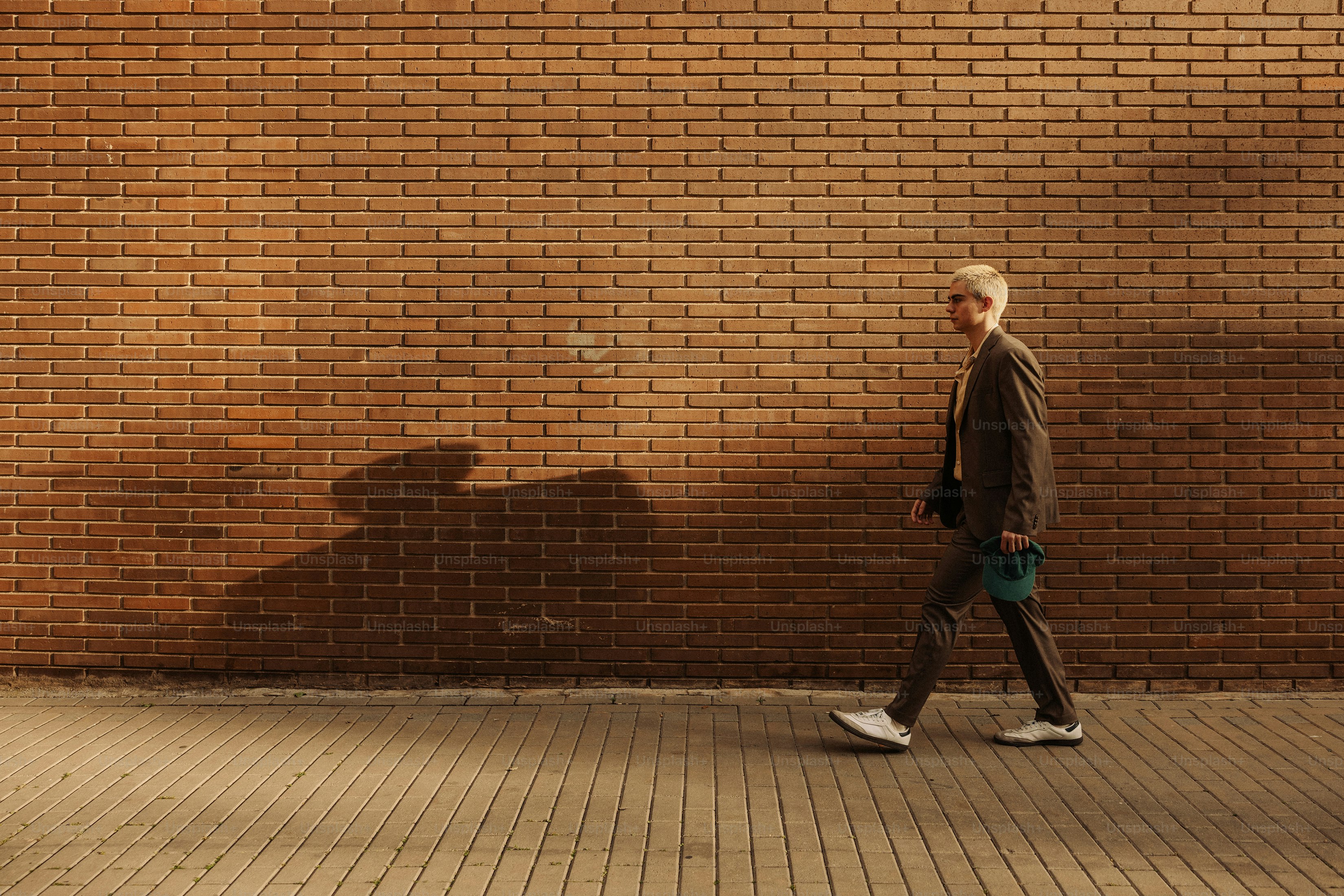 A person in a suit walks beside a brick wall.