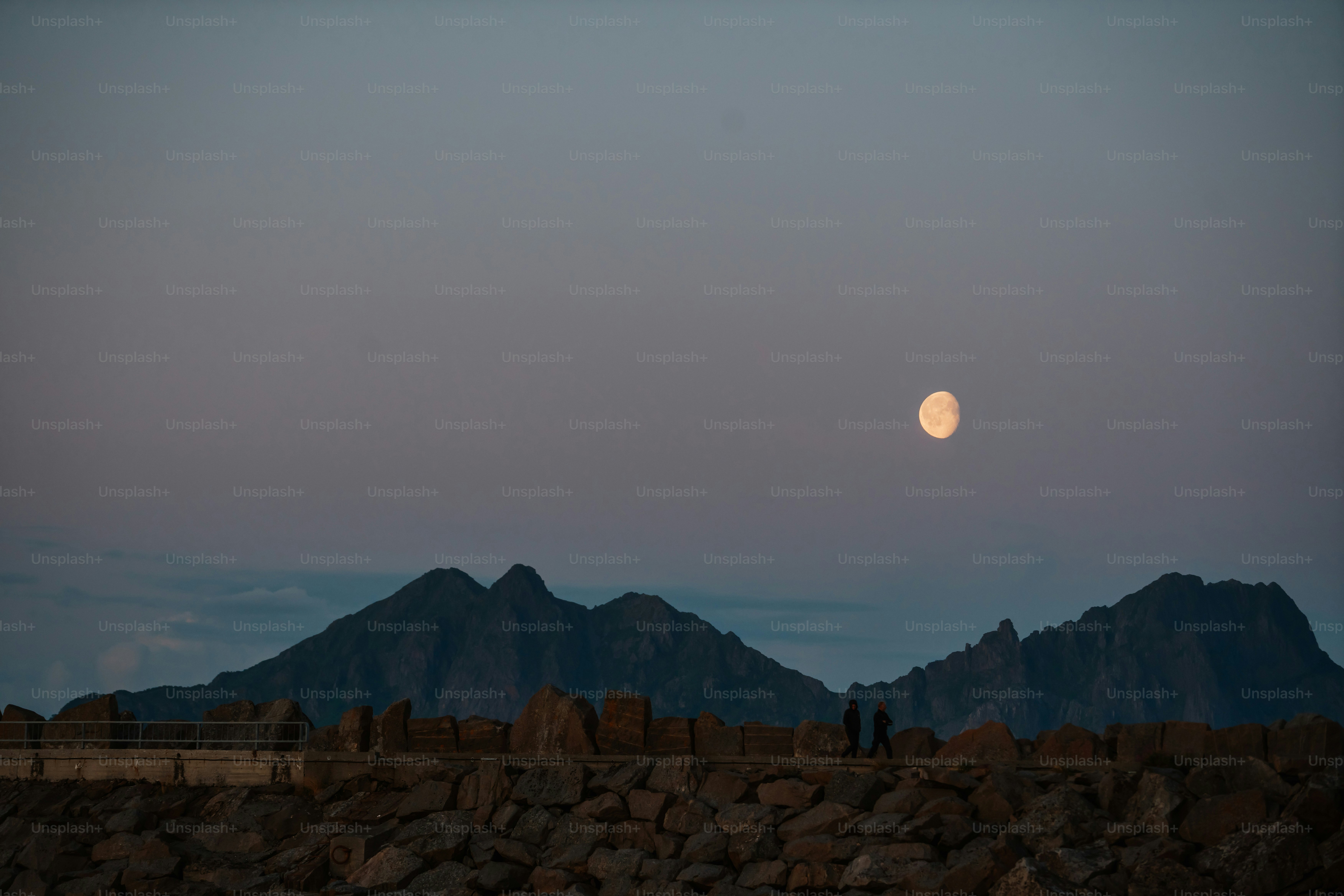 Full moon rises over silhouetted mountains at dusk