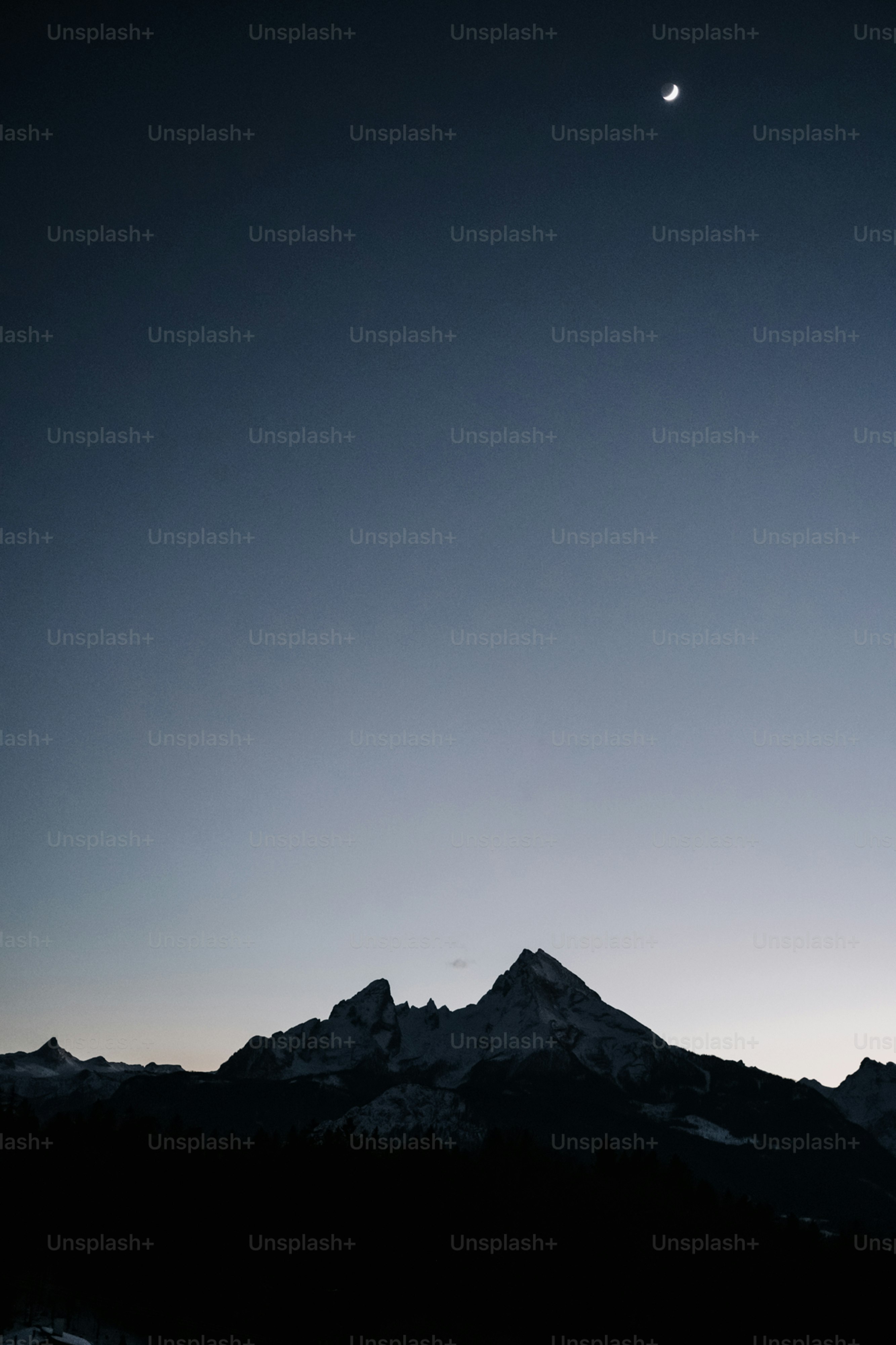 Crescent moon over silhouetted mountains at dusk
