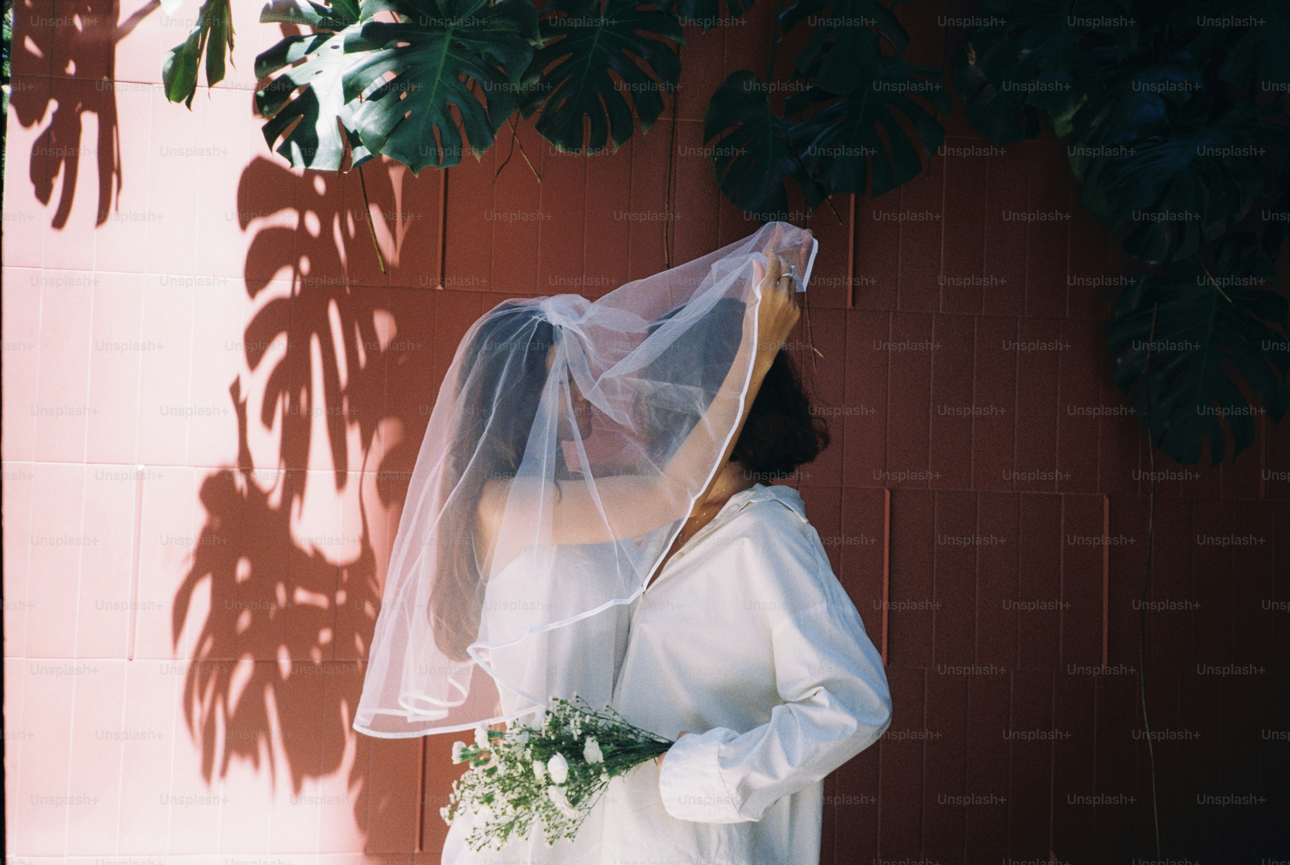 Woman in white dress holding veil and flowers.