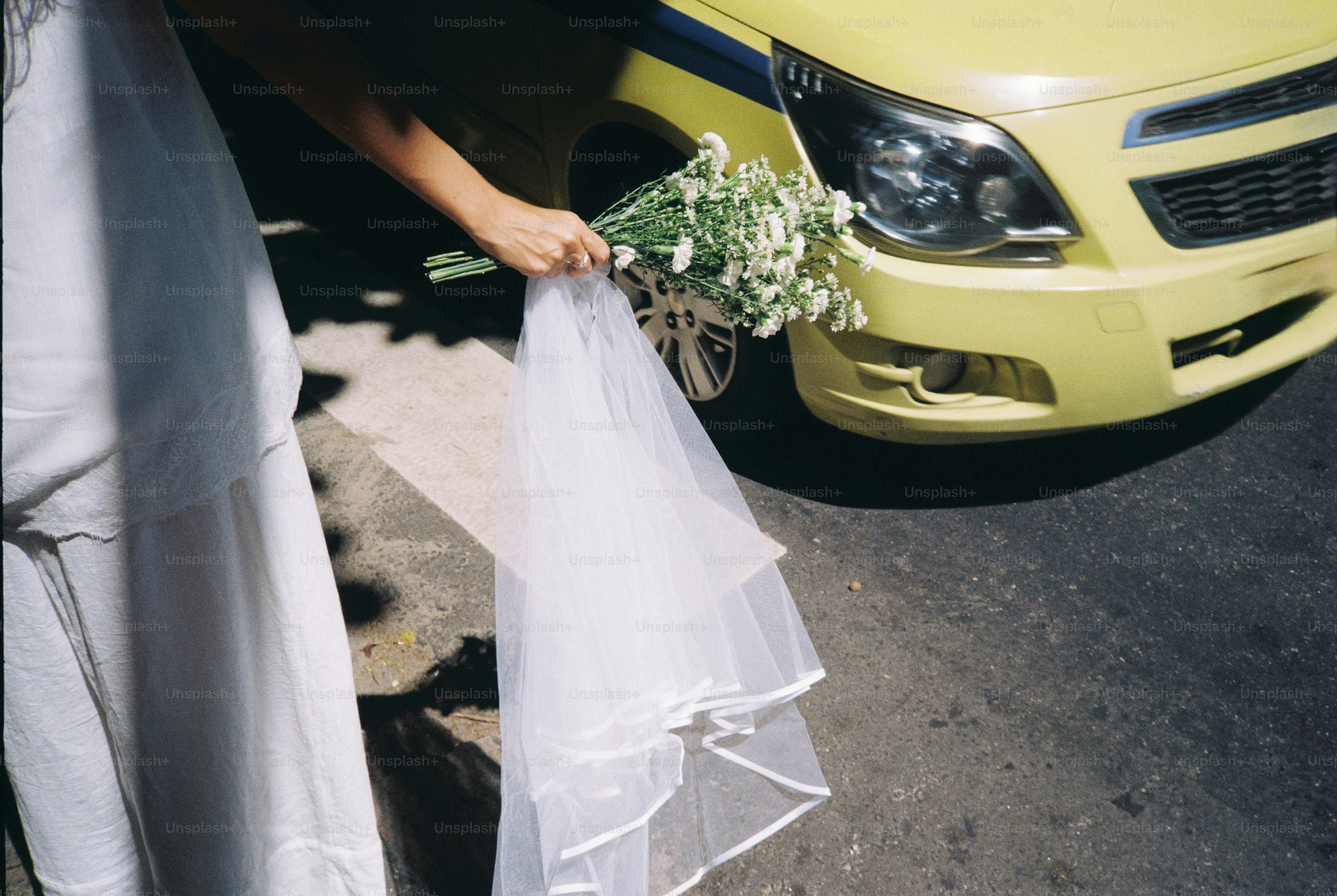 Bride holding bouquet and veil near yellow taxi