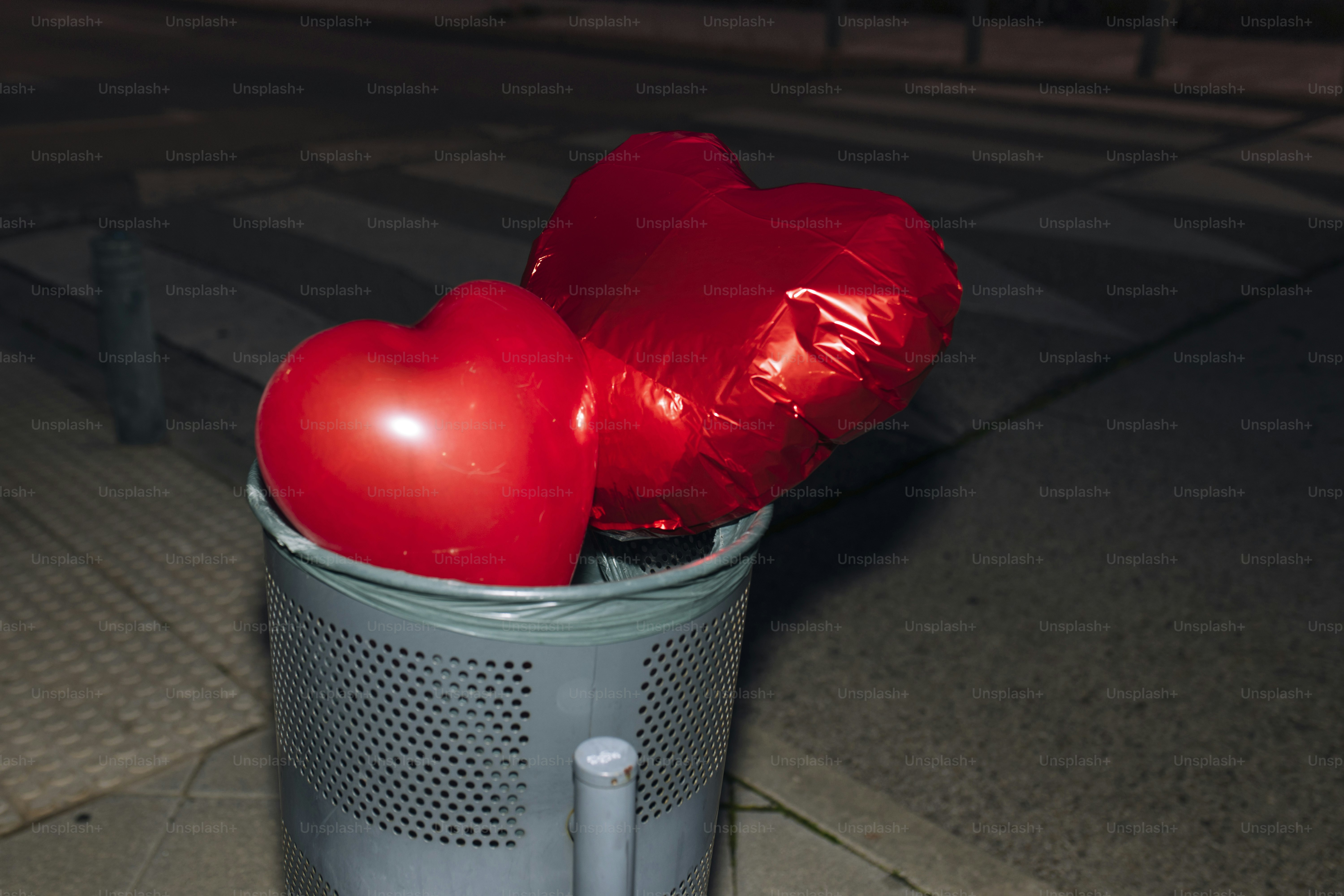 Two red heart balloons in a trash can