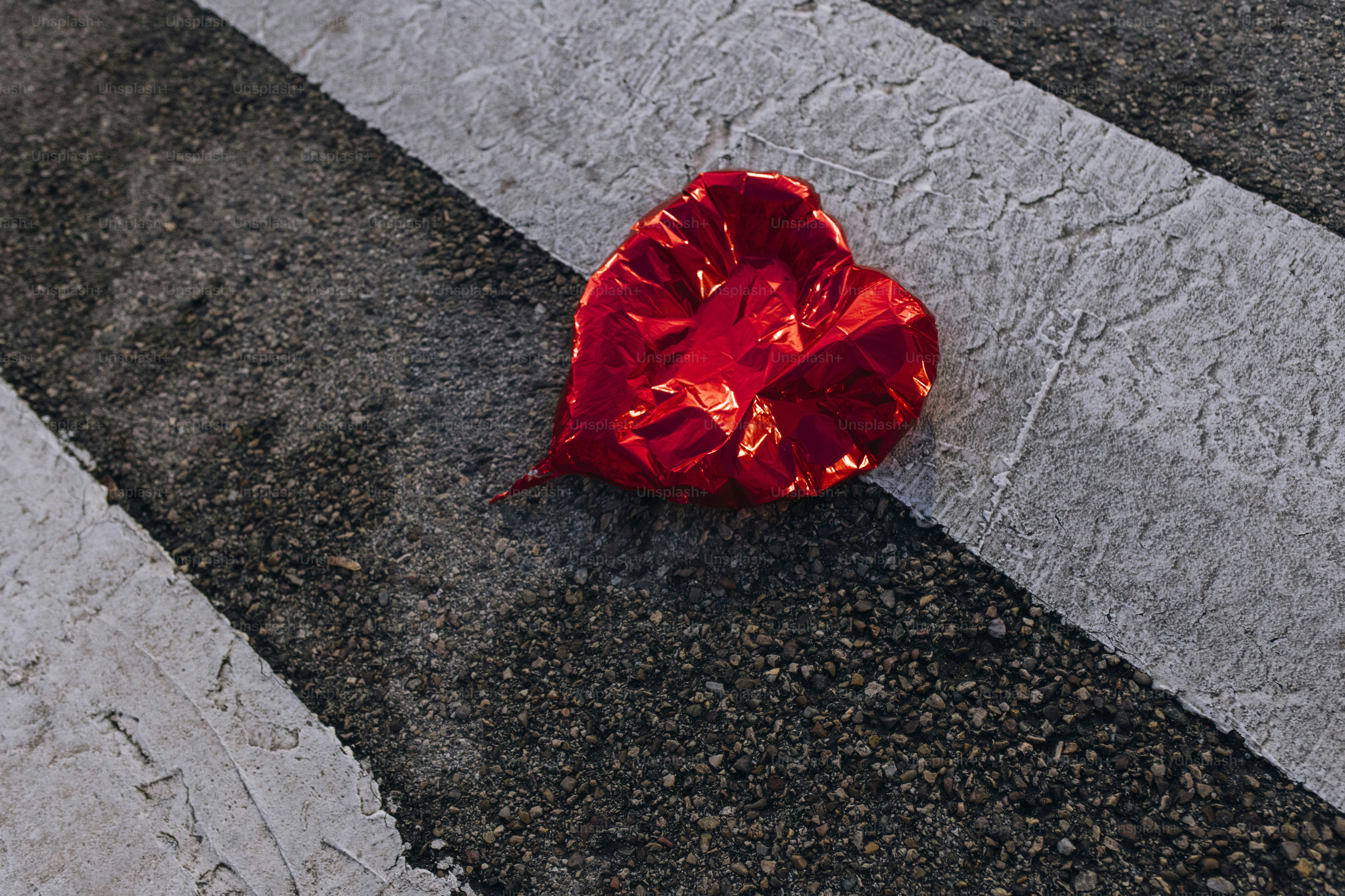 Deflated red heart balloon on crosswalk - Photo on Unsplash+
