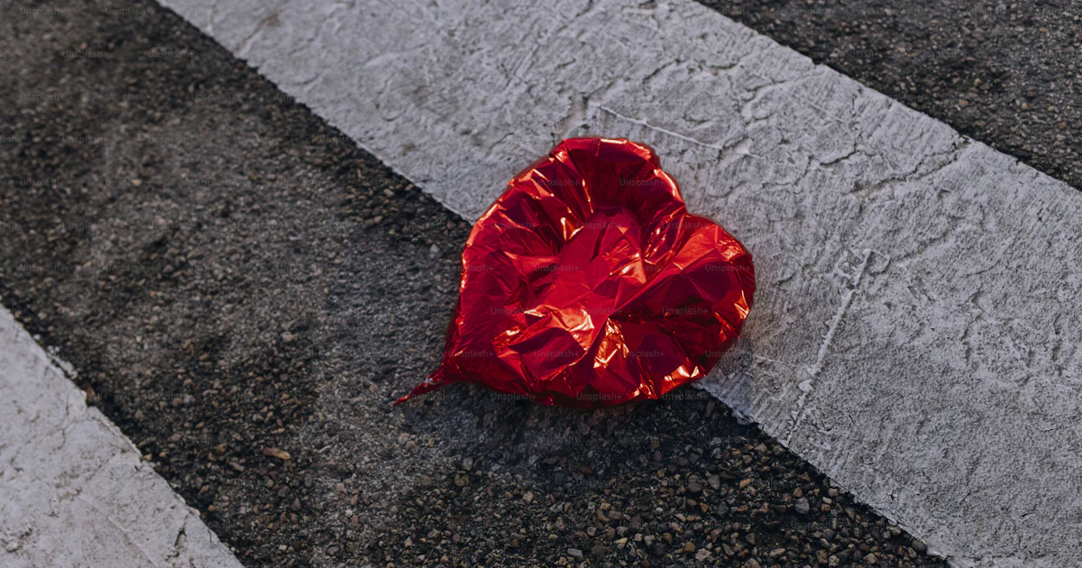 Deflated red heart balloon on crosswalk - Photo on Unsplash+