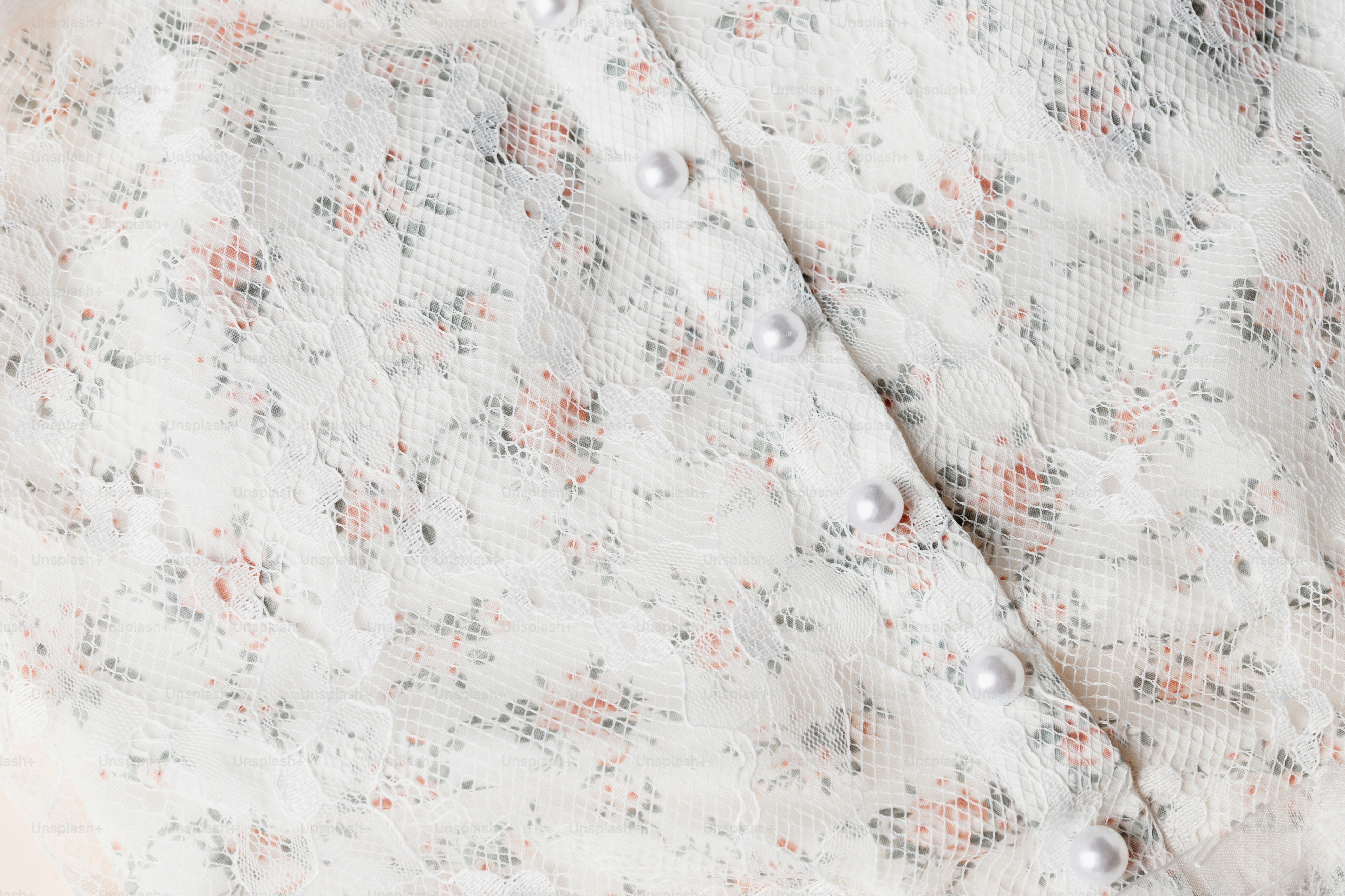 Close-up of a white floral lace fabric with pearl buttons.