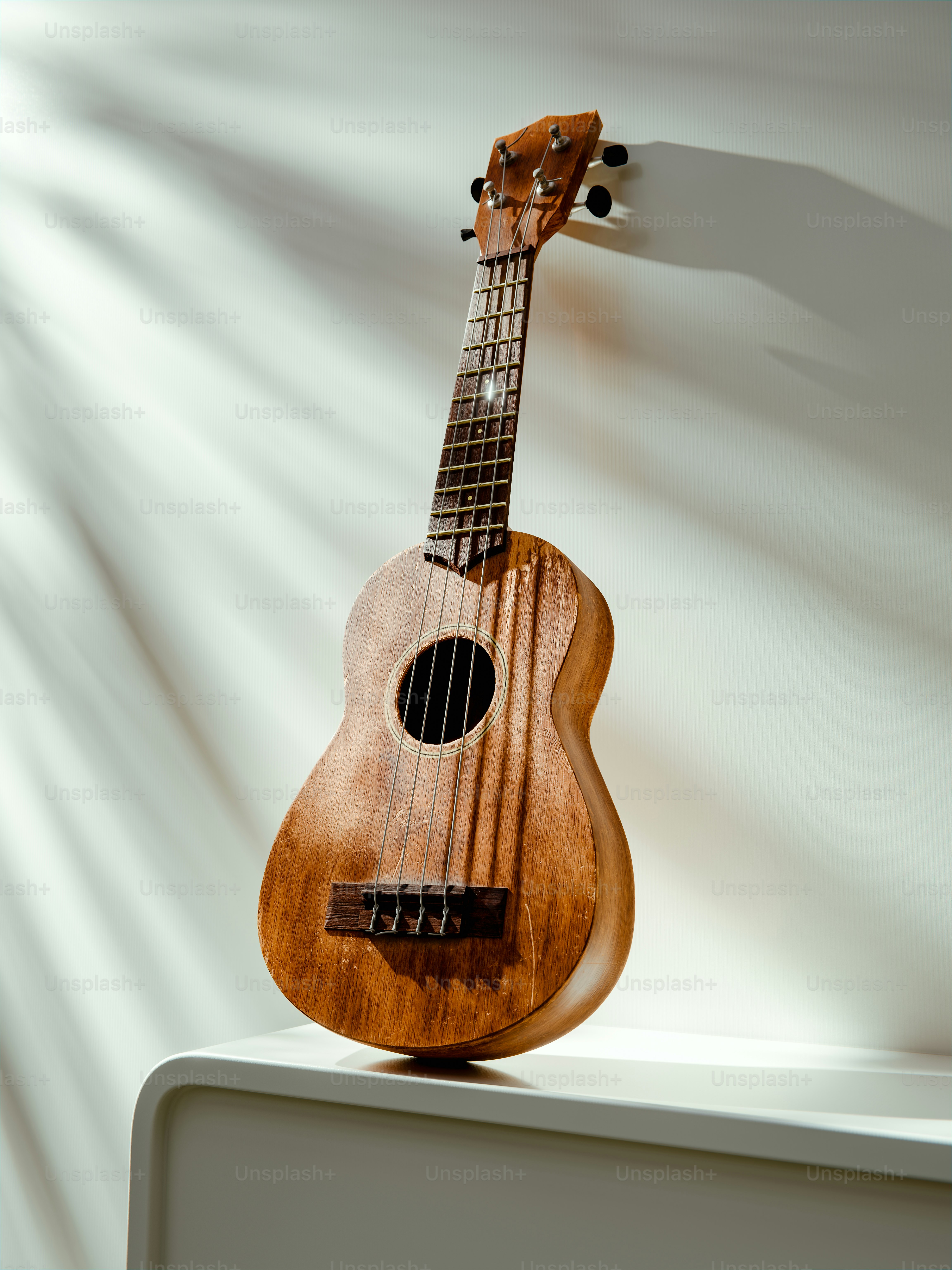 A wooden ukulele rests on a white surface.