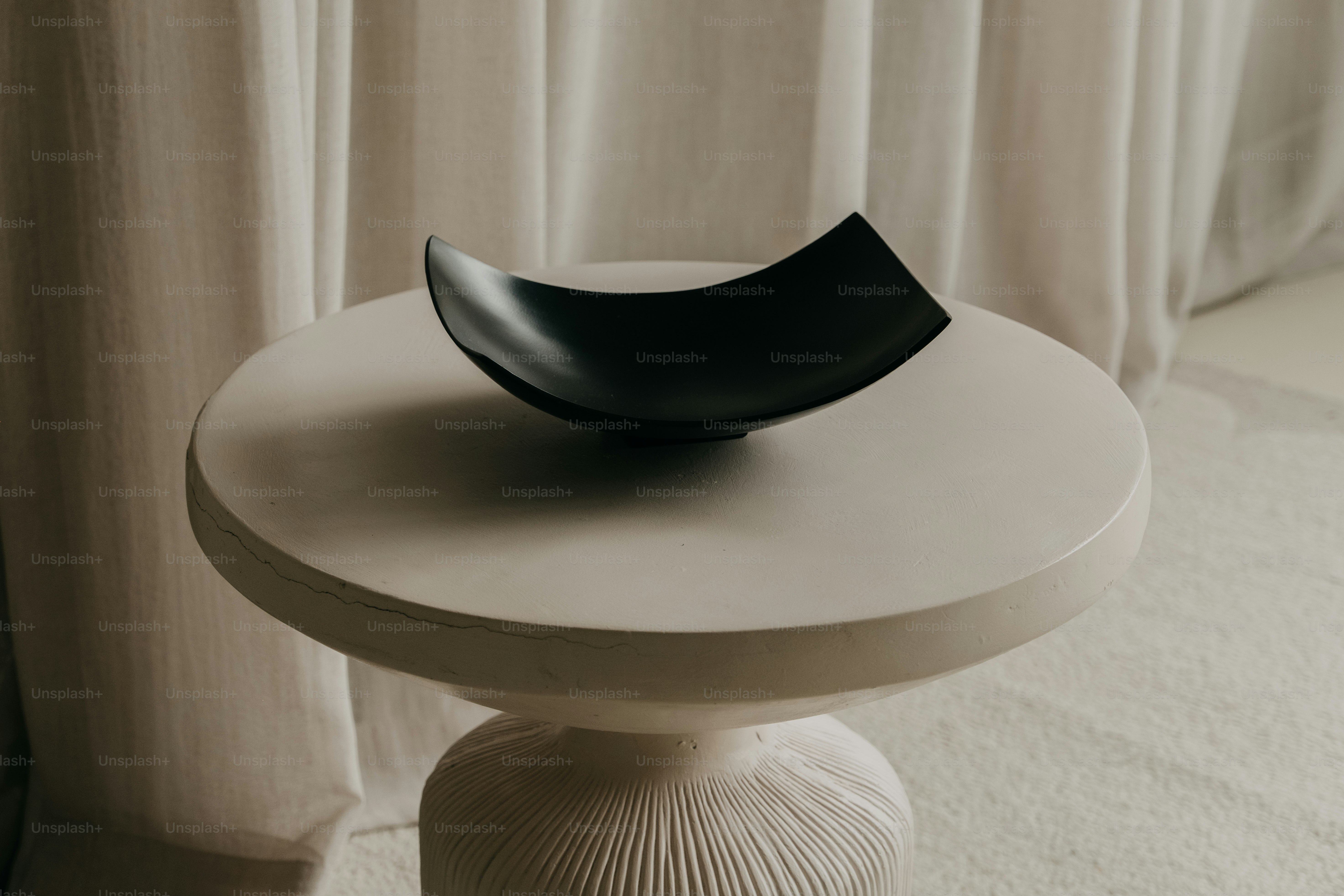 A black decorative bowl on a white pedestal table.