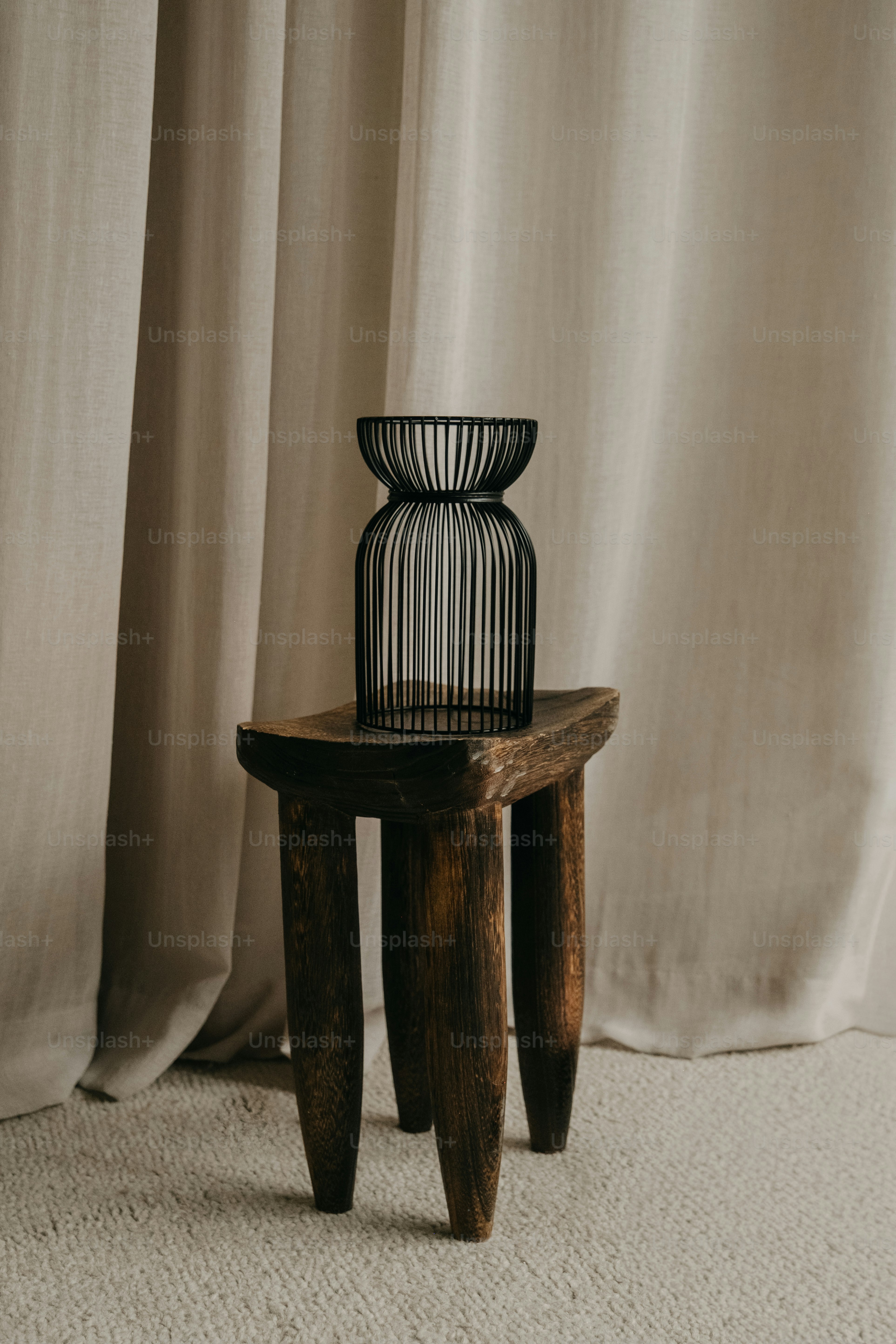 A black wire vase sits on a wooden stool.