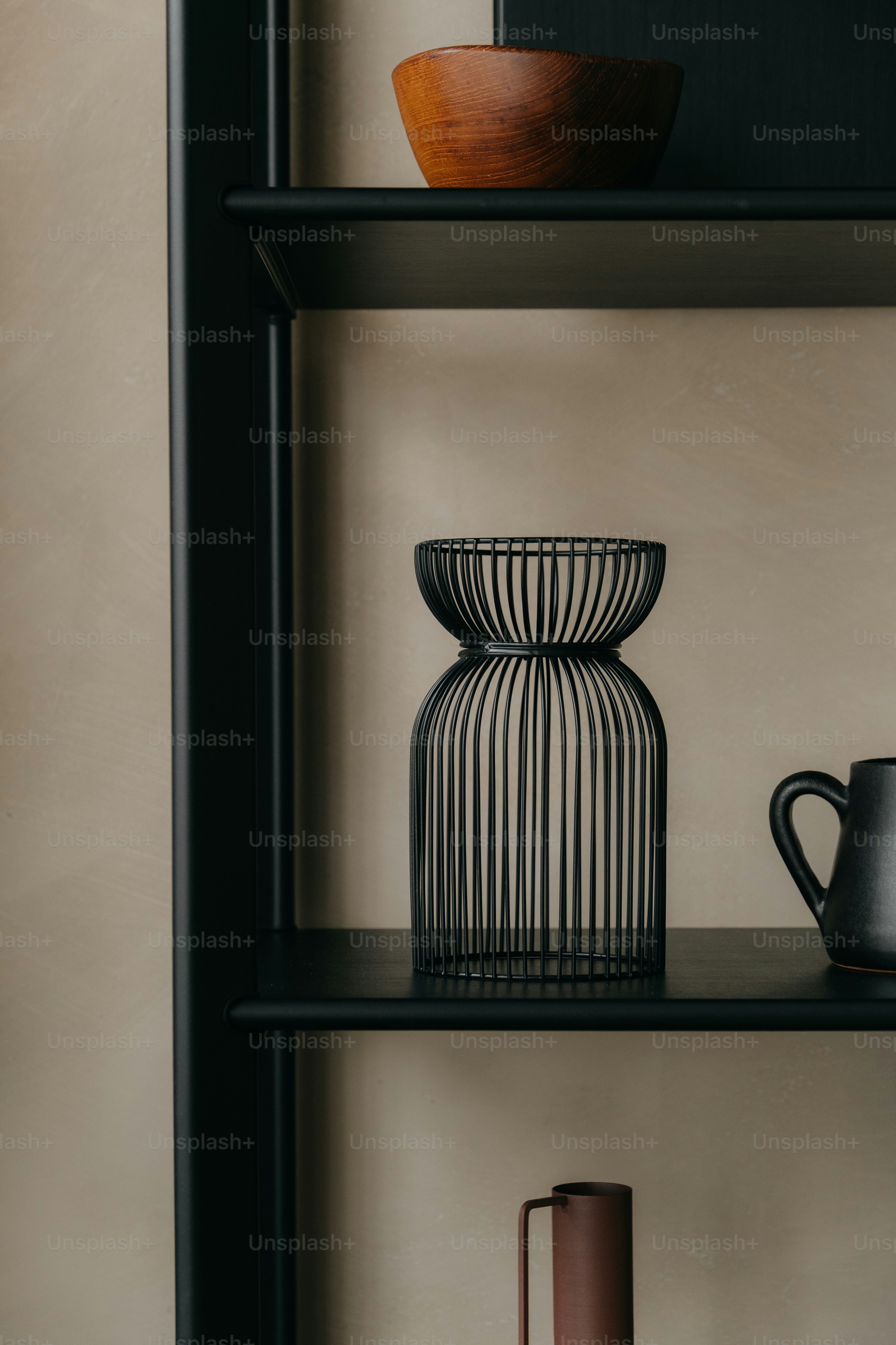 A black wire vase sits on a shelf.